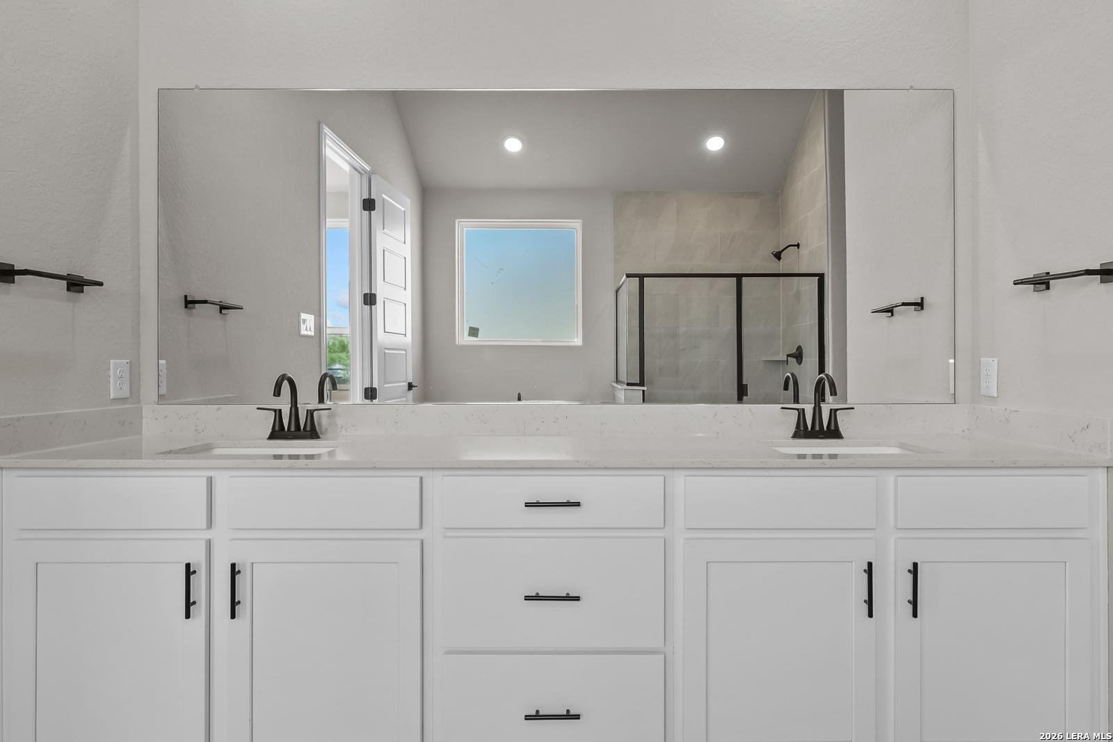 Dual vanity bathroom with white shaker cabinets, quartz countertops, matte black faucets, and large mirror in Davidson Homes Foster E plan