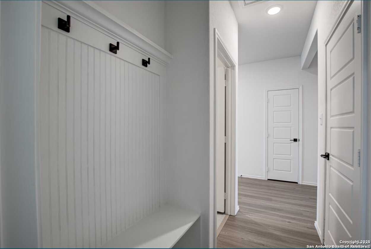 Bright entryway with white beadboard walls, coat hooks, bench, and wood flooring in Davidson Homes The Daphne H, Seguin, Texas
