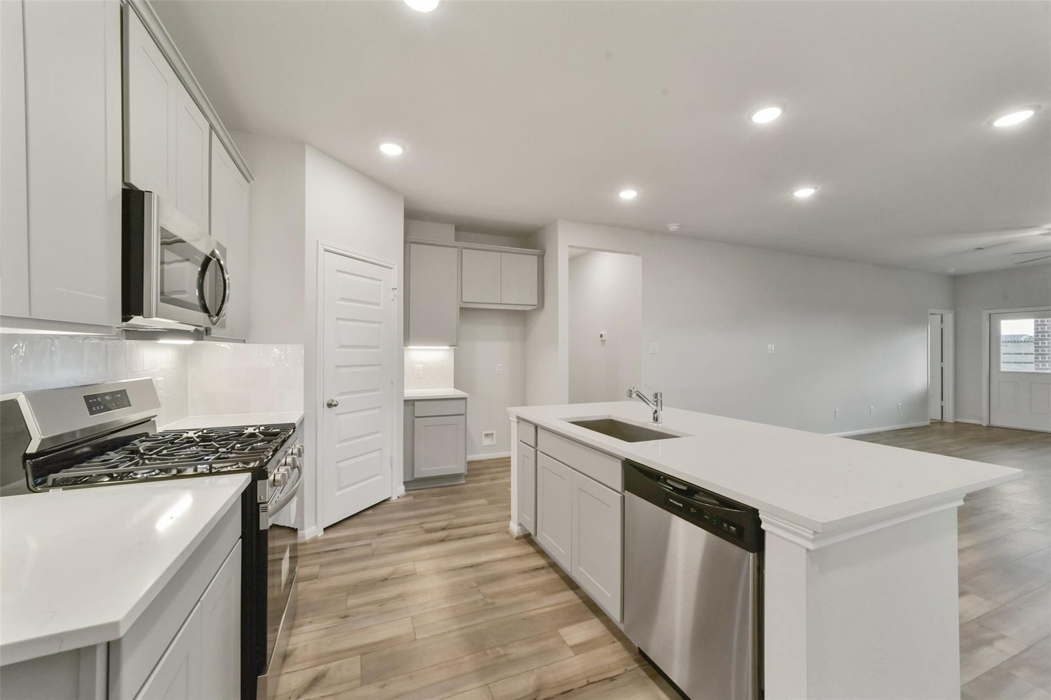 Modern white kitchen with stainless appliances, granite island sink, and hardwood floors in 5-bedroom San Marcos E home, Beasley, Texas