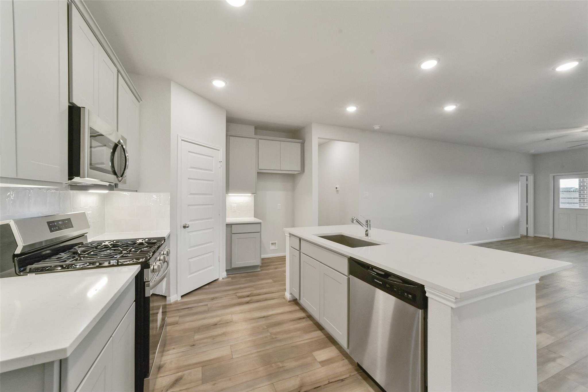 Modern white kitchen with stainless appliances, granite island sink, and hardwood floors in 5-bedroom San Marcos E home, Beasley, Texas
