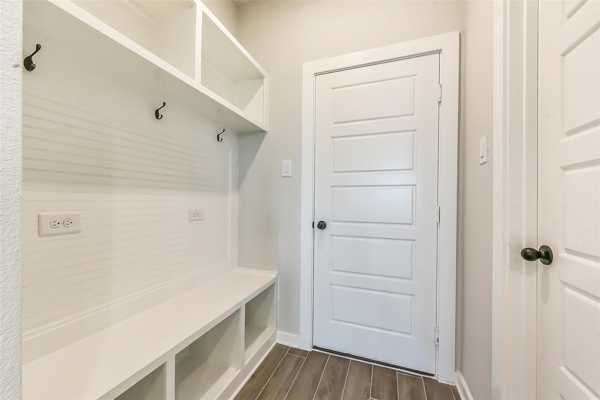 White shiplap mudroom with built-in bench, coat hooks, open shelves, and paneled door in Davidson Homes Sequoia C, Crosby Texas