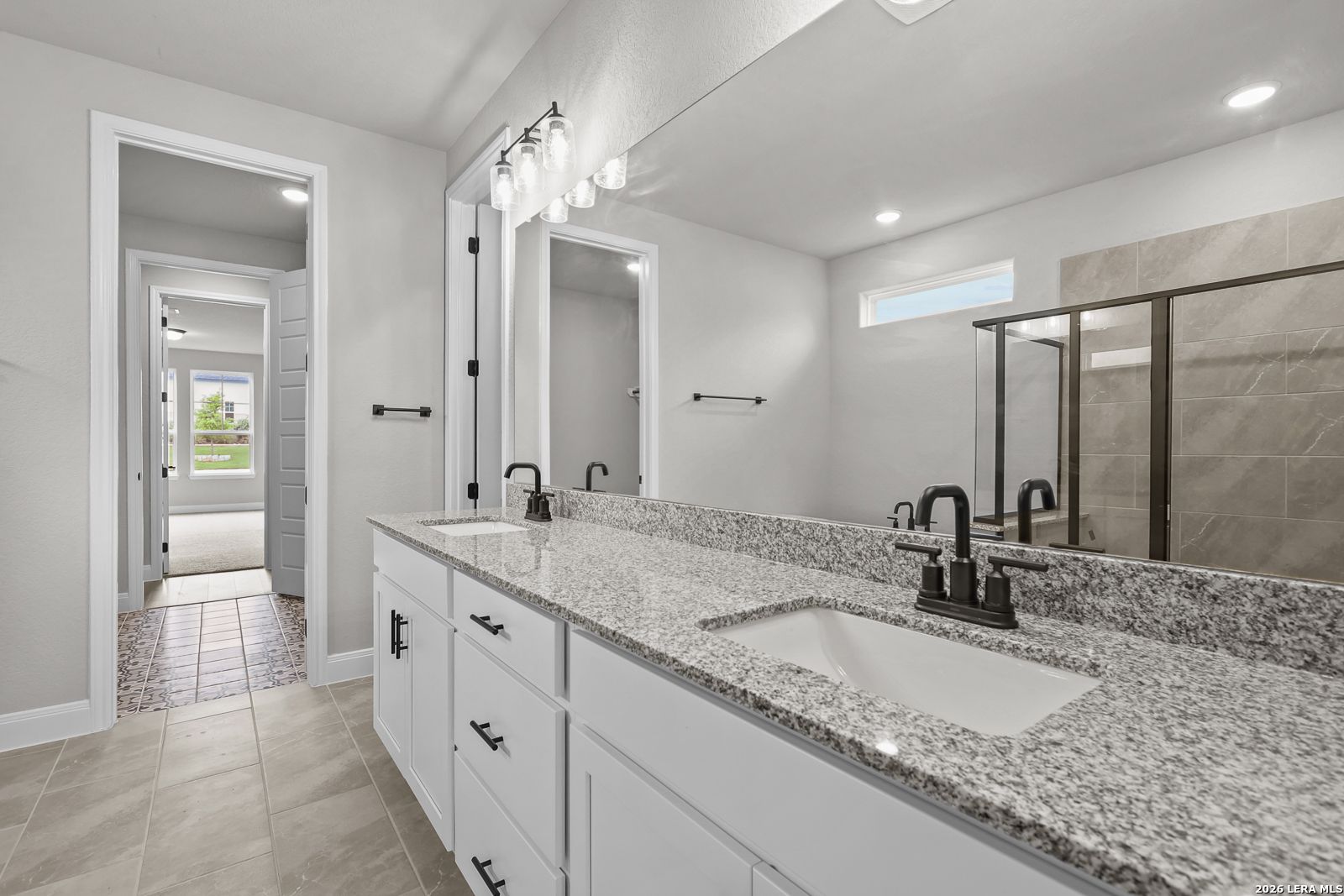 Modern master bath double vanity with granite counters, white cabinets, and glass shower in Davidson Homes Belmont H, Castroville TX