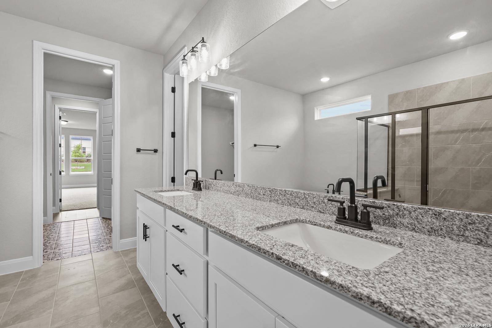 Modern master bath double vanity with granite counters, white cabinets, and glass shower in Davidson Homes Belmont H, Castroville TX