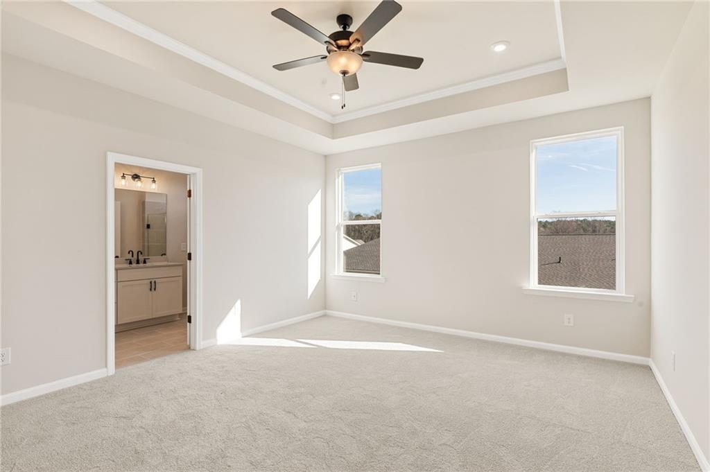 Bright bedroom with ceiling fan, large sunny windows, and open bathroom door in Davidson Homes The Glenwood A, Loganville, Georgia