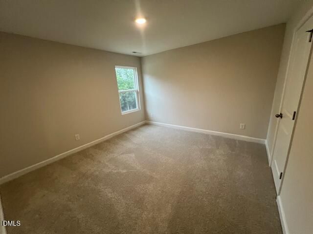 Empty bedroom with beige carpet, neutral walls, and window with wooded view in Davidson Homes The Willow D, Lillington NC