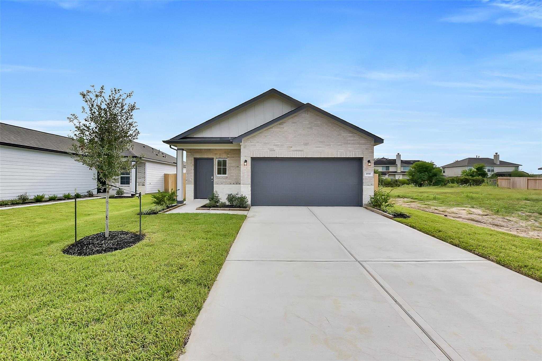 Modern 1-story beige brick home with 2-car gray garage, driveway, and lush green lawn in The Villages at WestPointe, Dayton, Texas