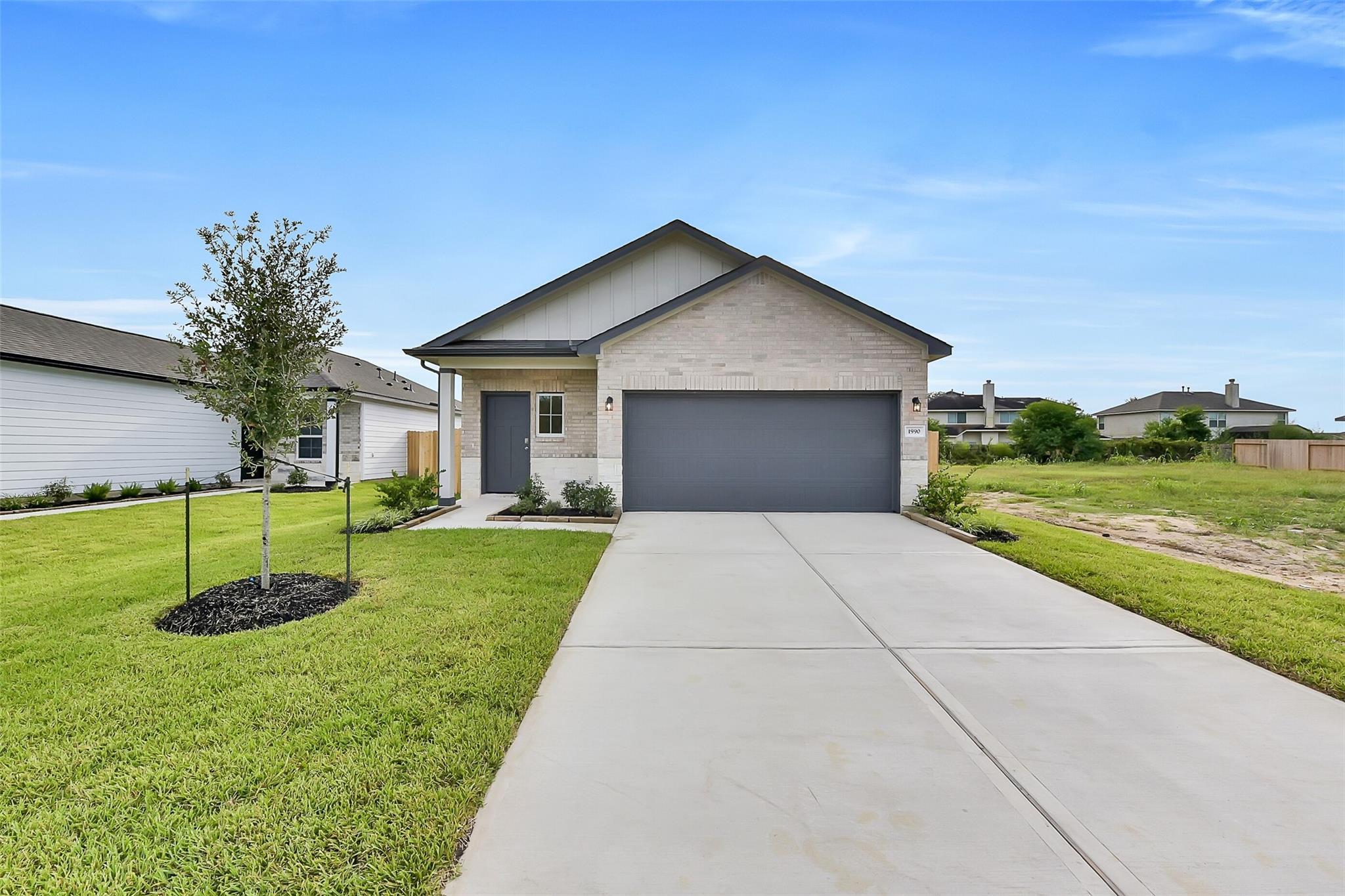 Modern 1-story beige brick home with 2-car gray garage, driveway, and lush green lawn in The Villages at WestPointe, Dayton, Texas