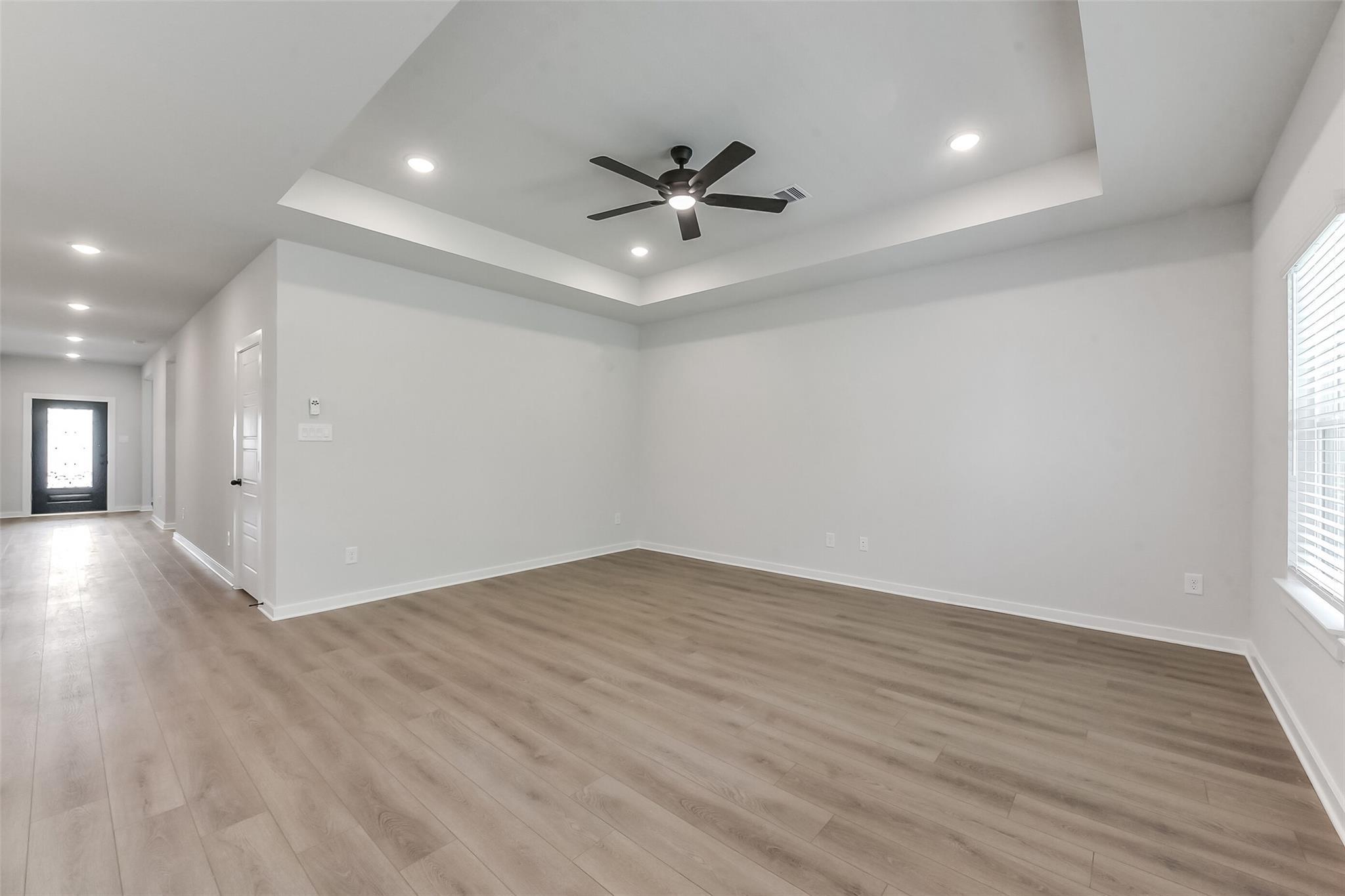 Spacious living room with tray ceiling, recessed lights, ceiling fan, and light wood floors in The Everett C, Crosby, Texas
