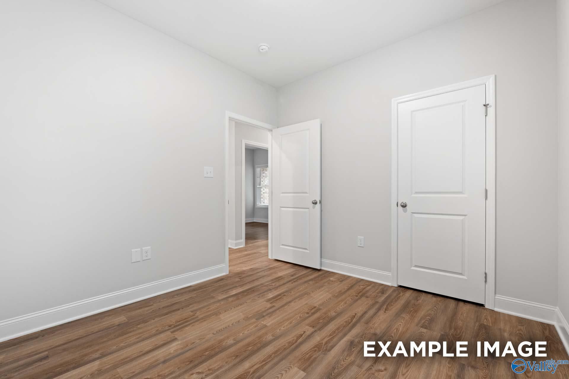 Bright secondary bedroom with hardwood floors, white walls, and open door in Davidson Homes The Cumberland, Decatur, AL