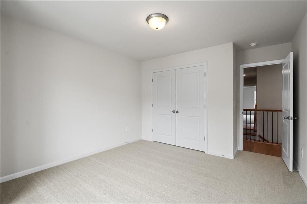 Bright secondary bedroom with double closet doors, beige carpet, and loft railing overlook in Davidson Homes The Marion B, Kennesaw, GA