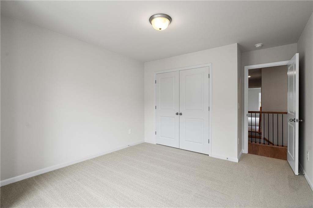 Bright secondary bedroom with double closet doors, beige carpet, and loft railing overlook in Davidson Homes The Marion B, Kennesaw, GA