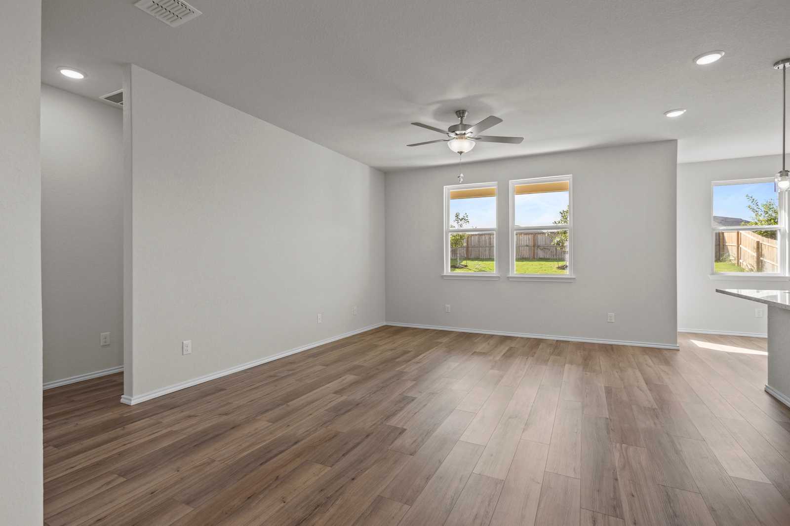 Open living room with hardwood floors, ceiling fan, large windows to grassy backyard in The Redbud B by Davidson Homes, Josephine, TX