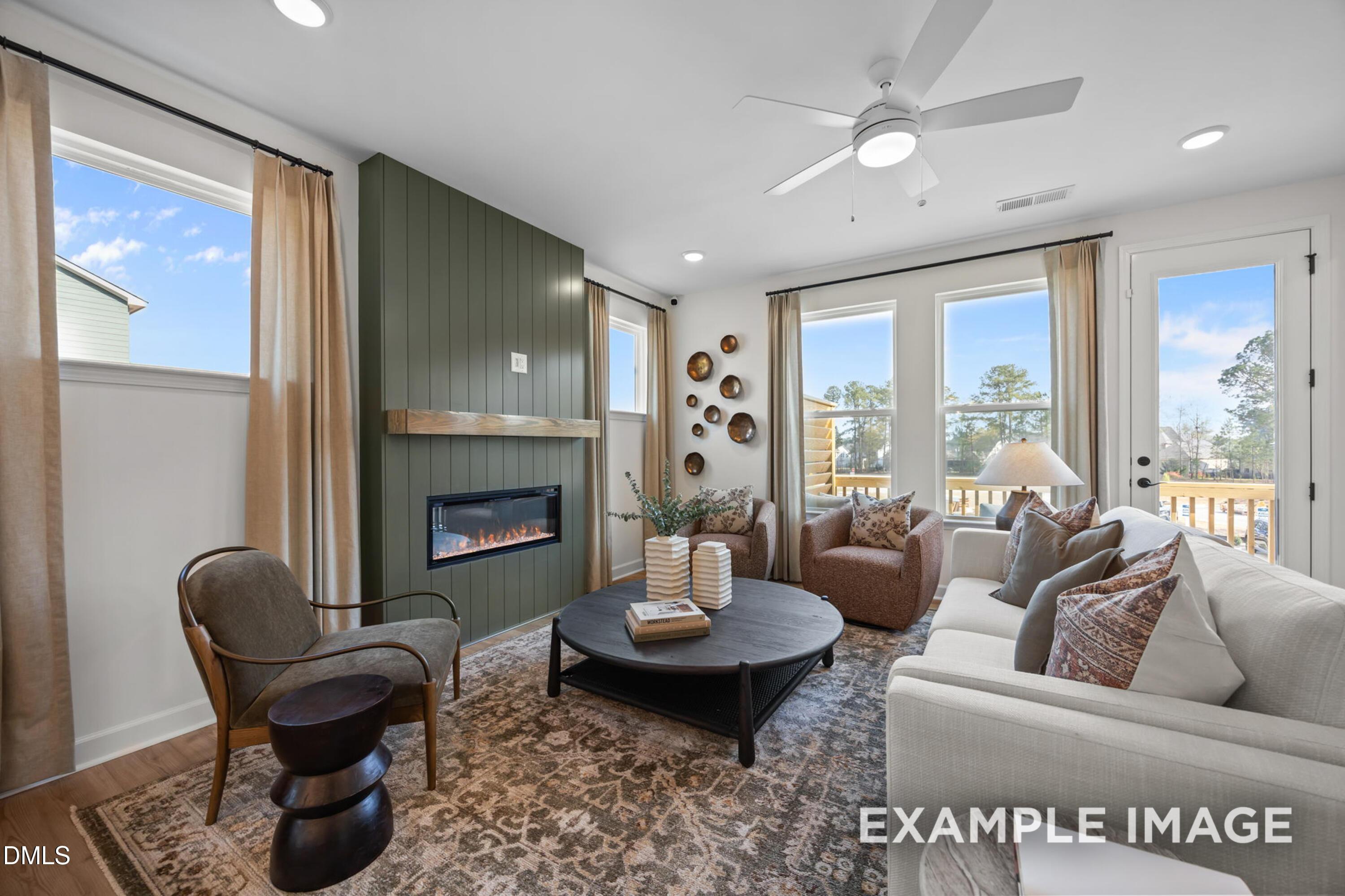 Cozy living room with gas fireplace, beige sofa, velvet armchair, and large windows in Davidson Homes The Mitchell, Knightdale, NC