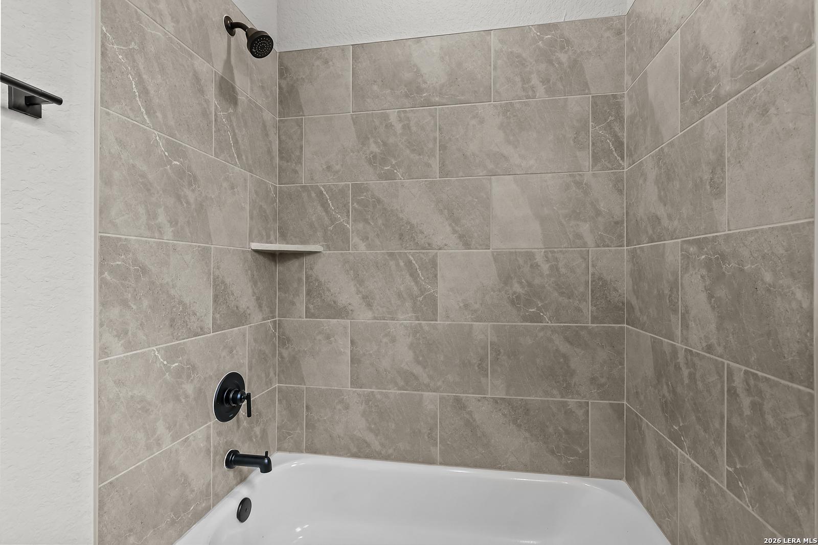 Modern gray marble tile shower and soaking tub with black fixtures in Davidson Homes The Belmont H, Castroville, Texas
