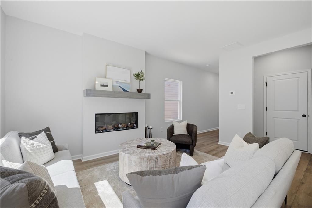 Bright great room with linear fireplace, wood-look floors, and neutral seating in The Hartwell C plan at The Bluffs, Canton, GA