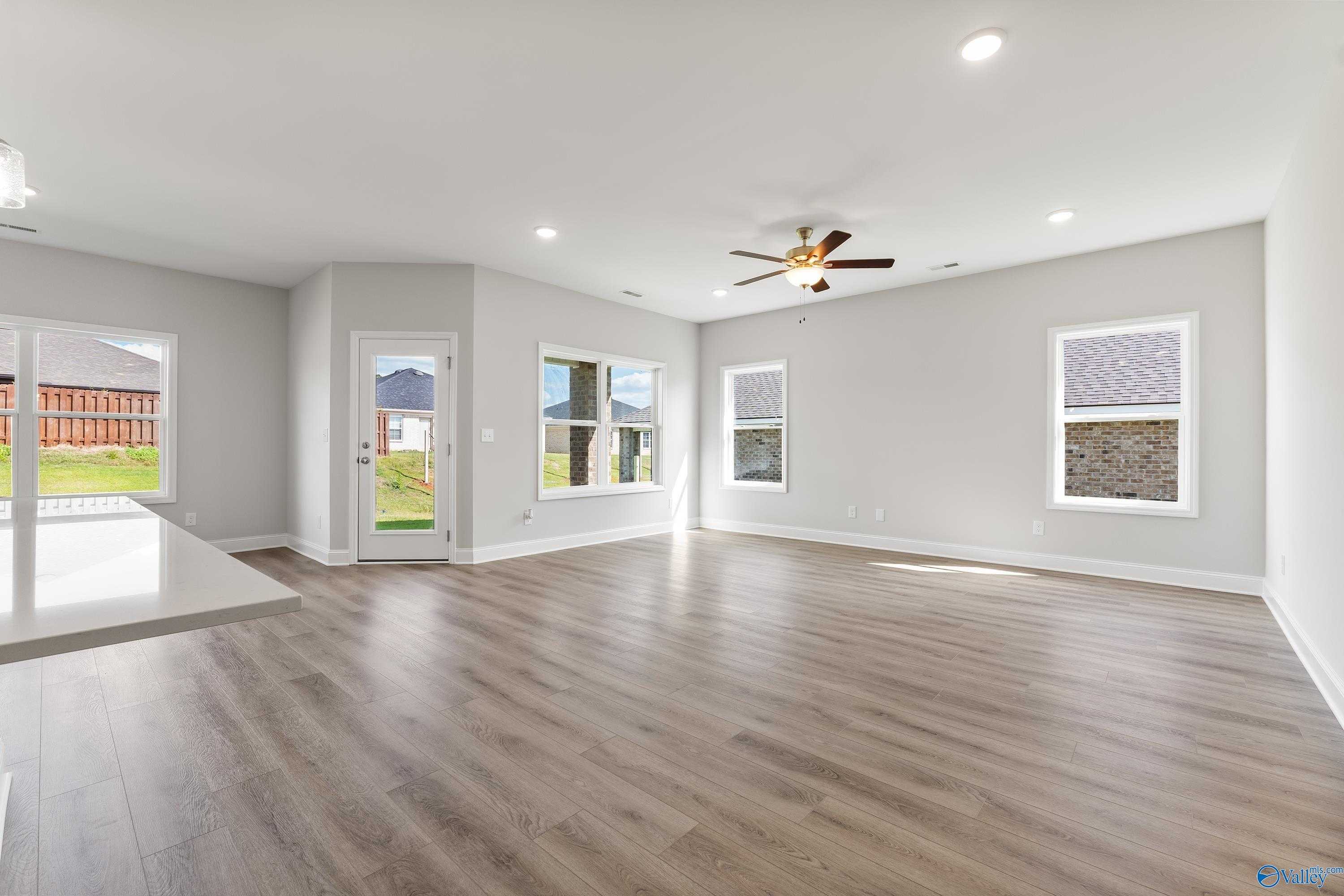 Open living room with hardwood floors, ceiling fan, French doors to backyard, and large windows in Davidson Homes The Franklin C, Toney, Alabama