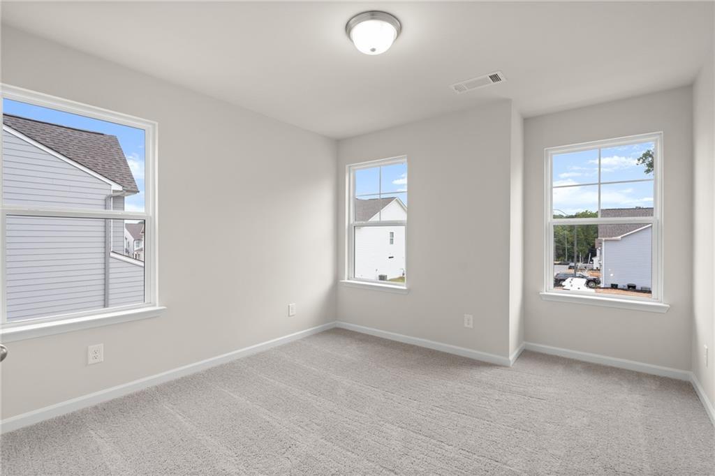 Bright secondary bedroom with light gray walls, beige carpet, large windows overlooking neighborhood in The Marion B, Kennesaw, Georgia