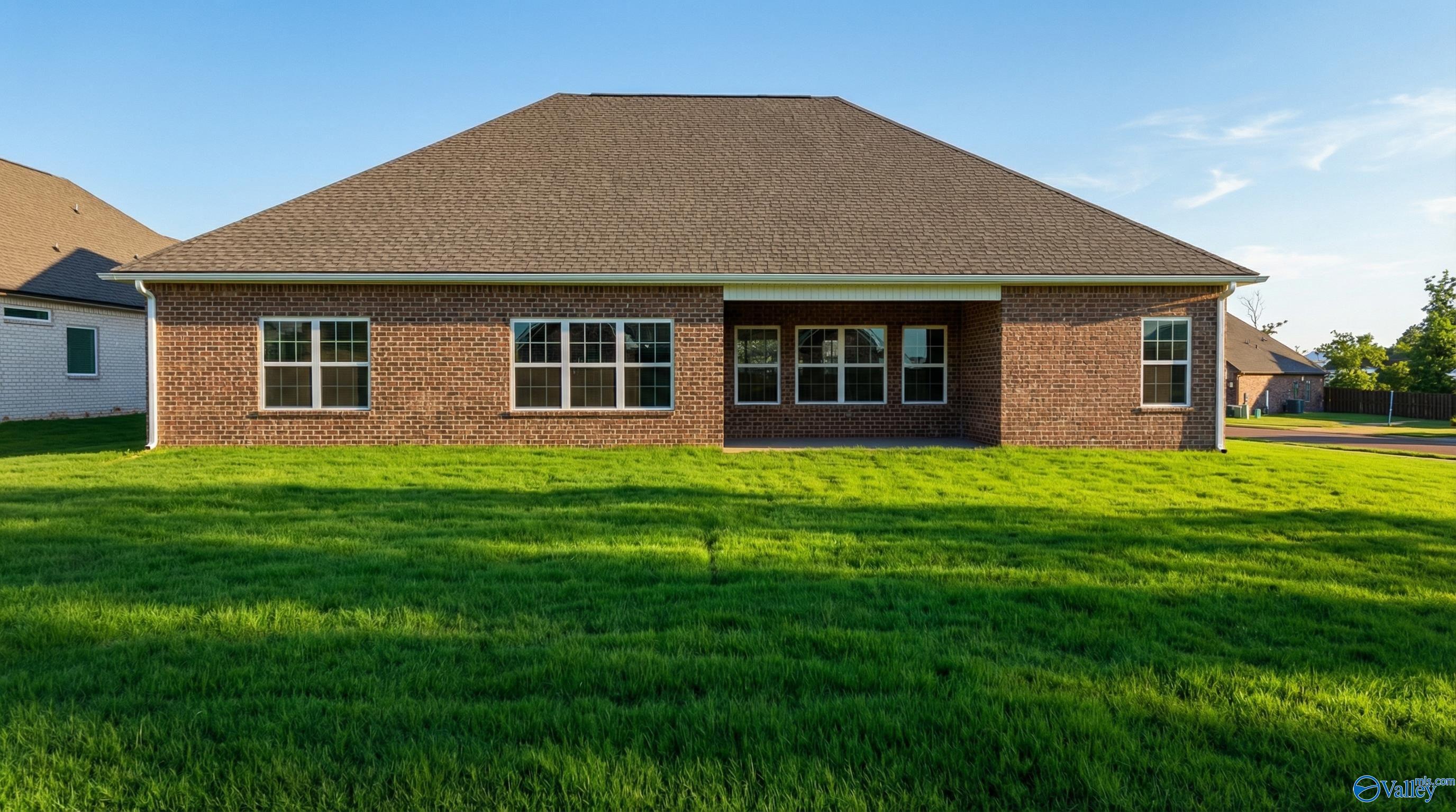 Rear view of brick single-story Davidson Homes Finleigh with covered patio, large windows, and lush green lawn in Creekside, Harvest, AL