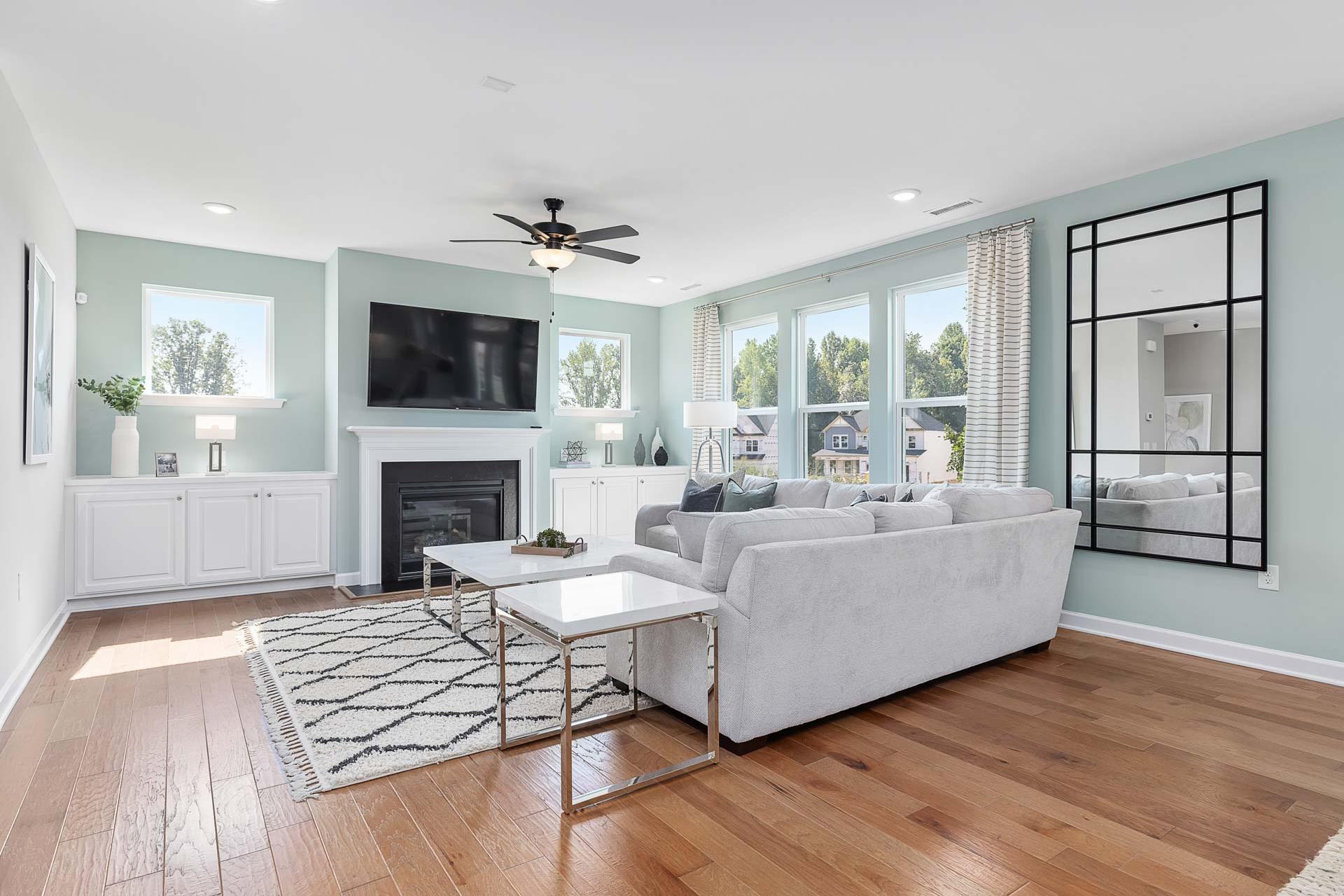 Spacious living room in Highland Forest by Davidson Homes, Fuquay-Varina NC with gas fireplace, gray sectional sofa, hardwood floors, large windows