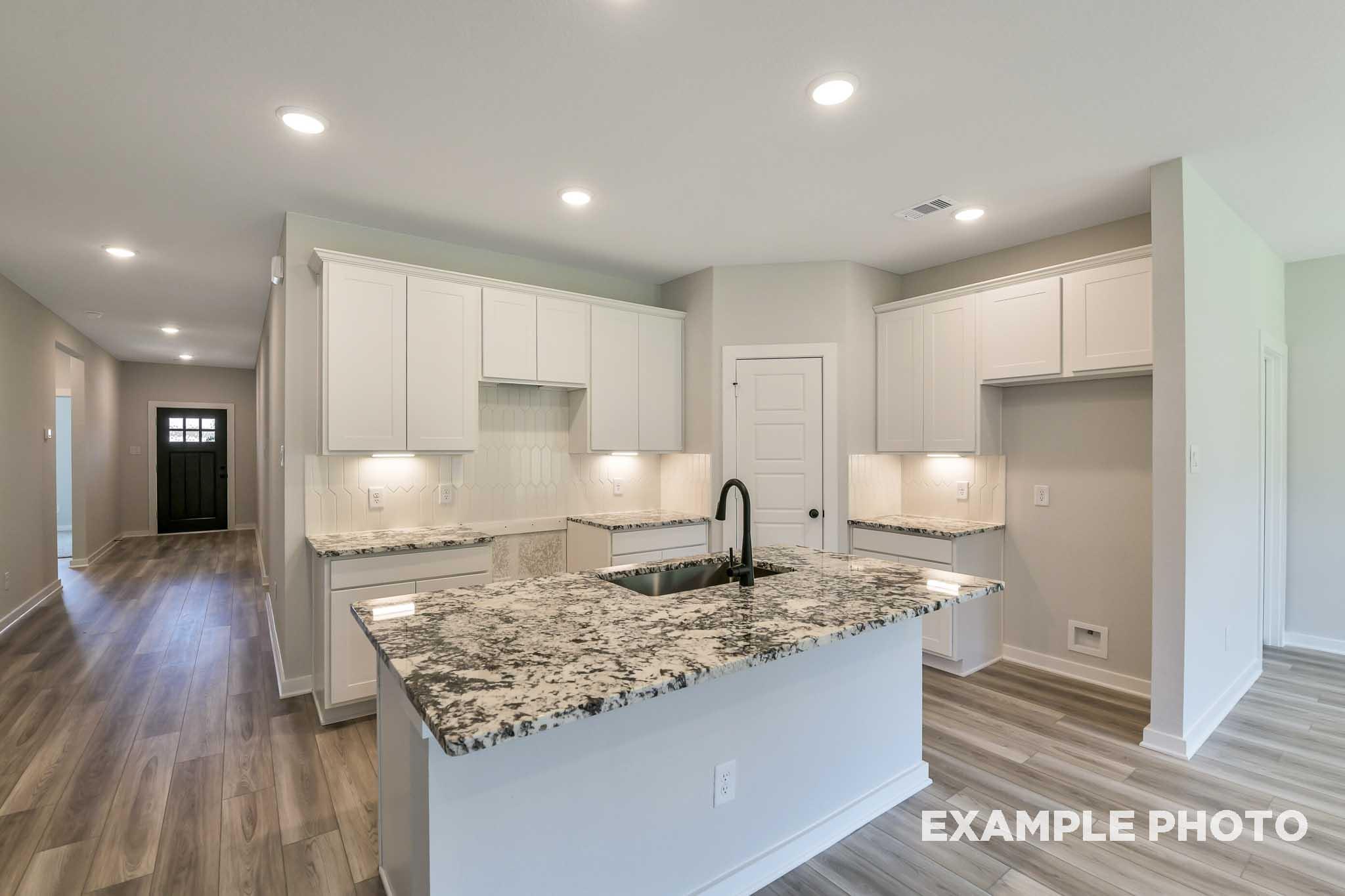 Spacious kitchen in The Daphne G featuring white shaker cabinets, speckled granite island with sink, hardwood floors, and open layout