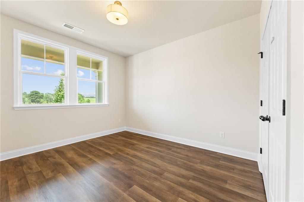 Sunny bedroom with hardwood floors, beige walls, double windows overlooking trees in Davidson Homes The Harrison H, Winder, GA