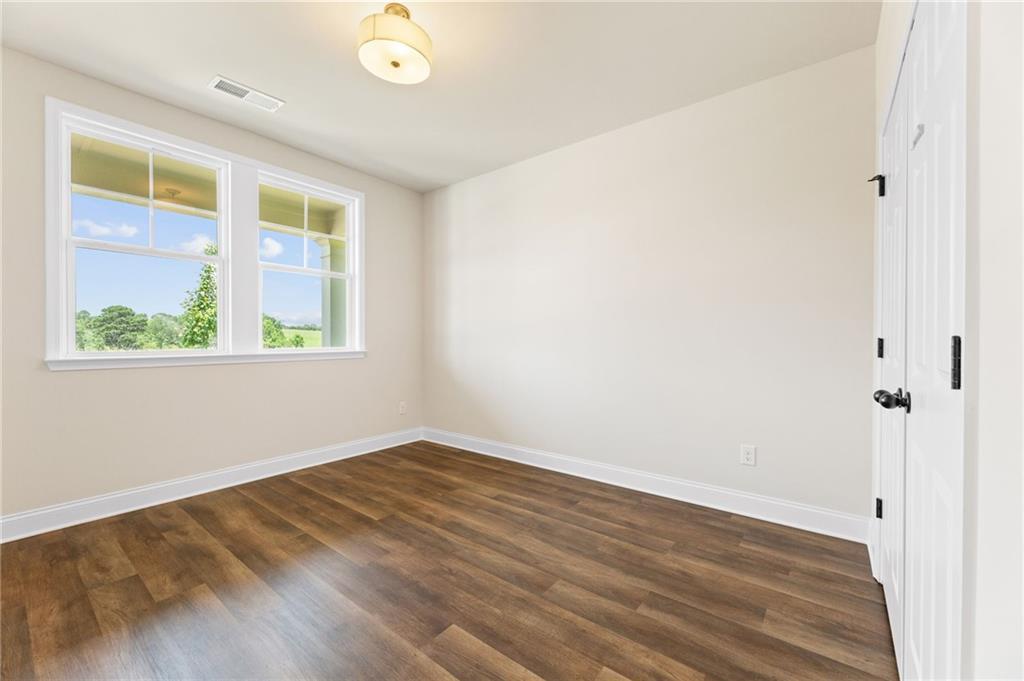 Sunny bedroom with hardwood floors, beige walls, double windows overlooking trees in Davidson Homes The Harrison H, Winder, GA