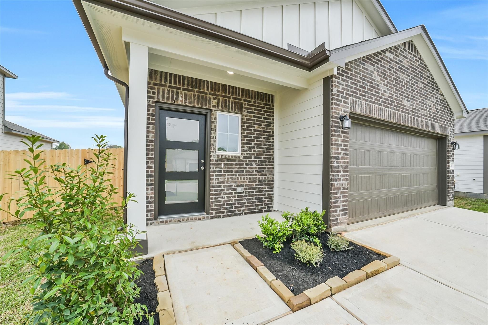 Modern brick facade of Davidson Homes The Frio F with covered porch, black door, 2-car garage in Conroe, Texas