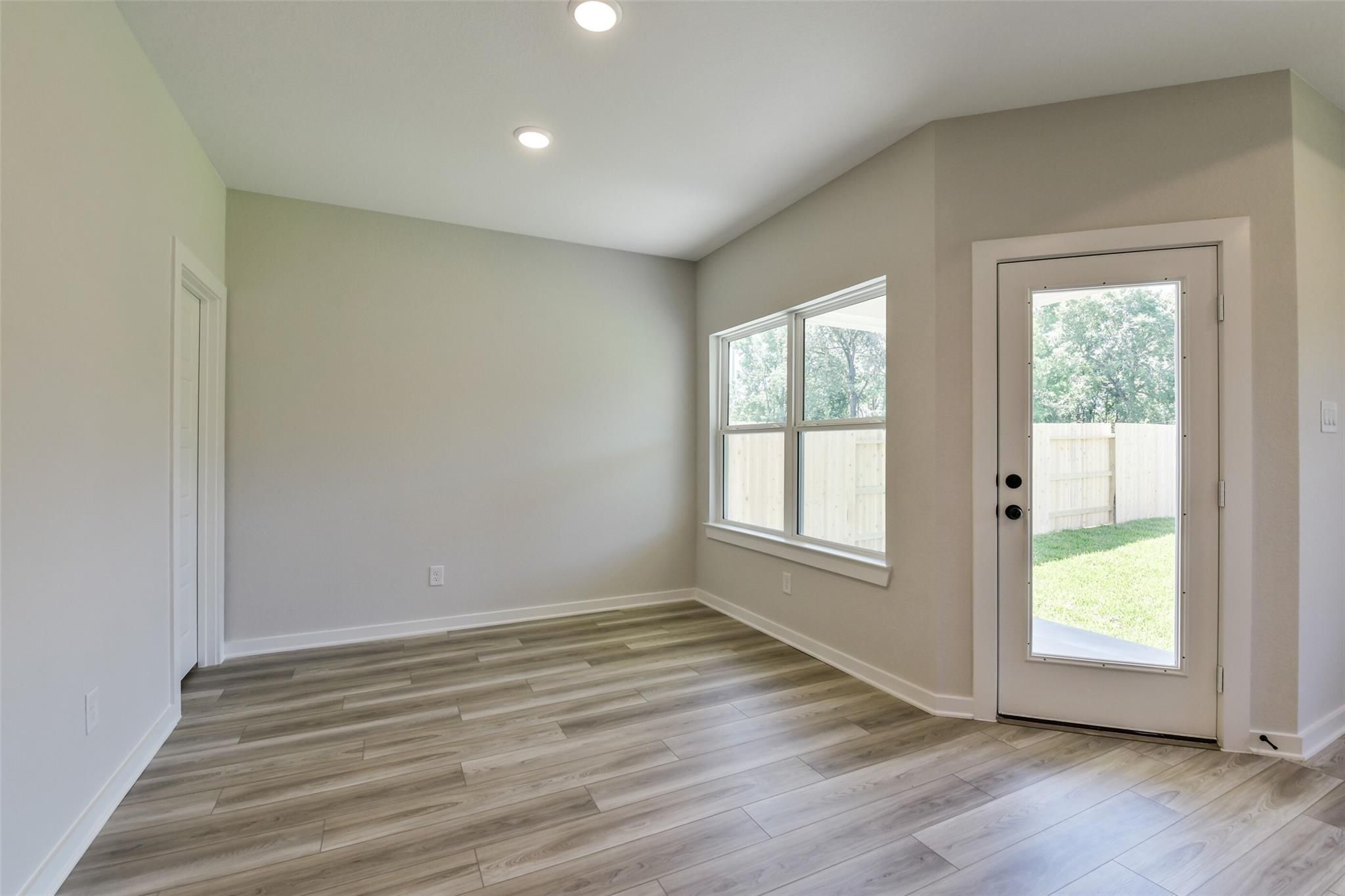 Bright living room with large windows, French door to lush backyard, hardwood floors in The Daphne H, Crosby Texas