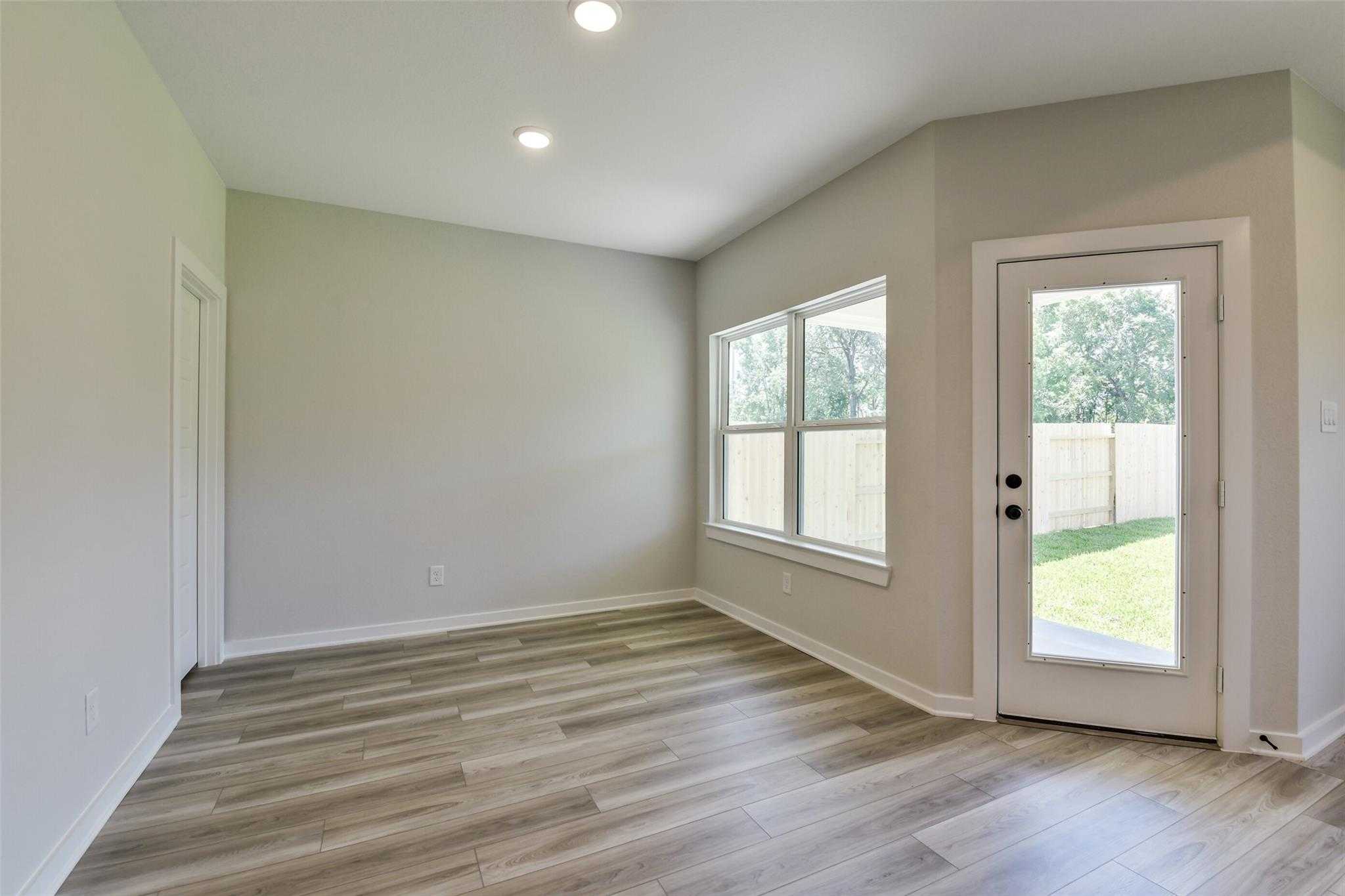 Bright living room with large windows, French door to lush backyard, hardwood floors in The Daphne H, Crosby Texas