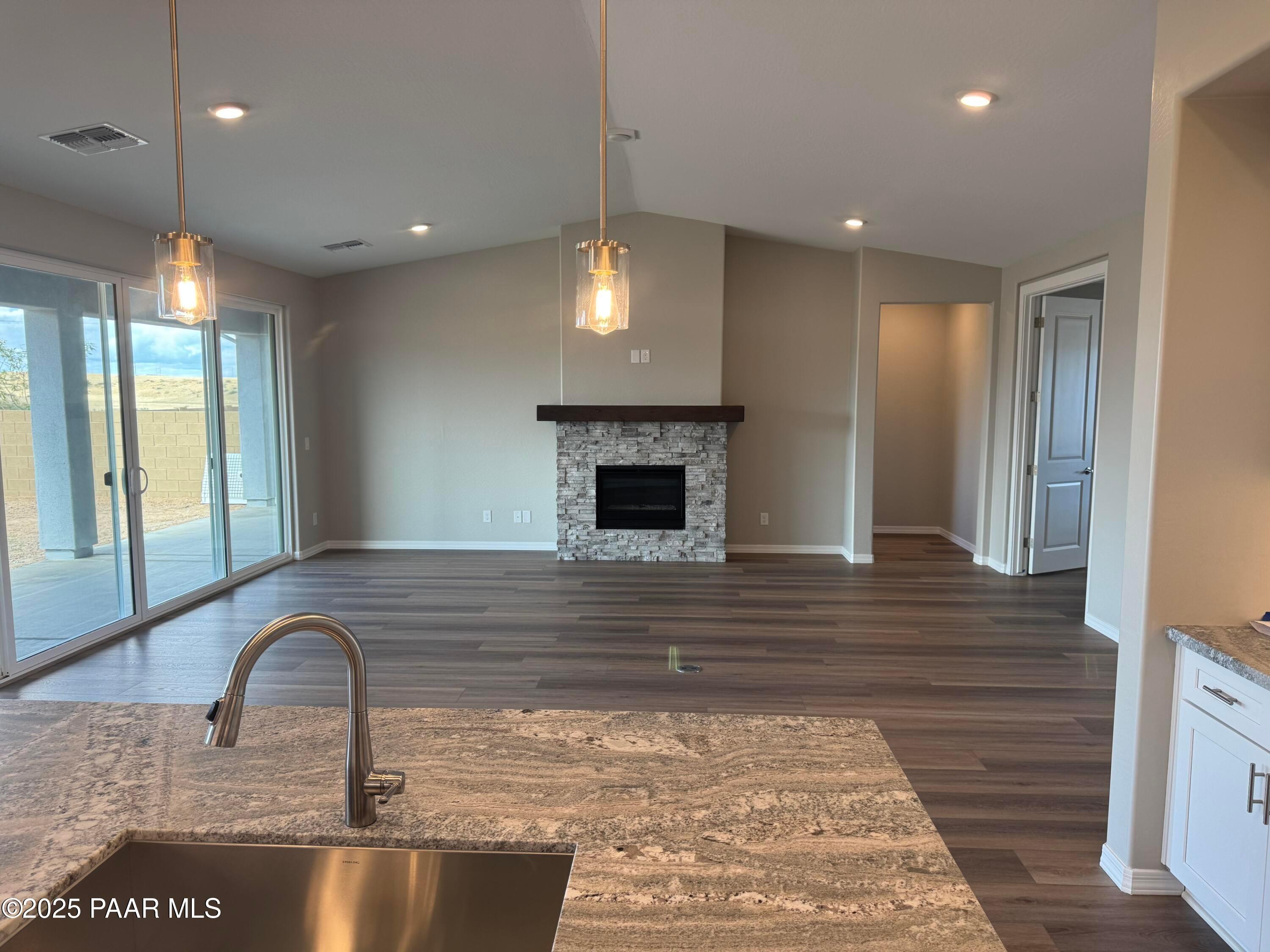 Open-concept living room with stacked stone fireplace, quartz kitchen island, and sliding glass doors to desert view in The Monarch A, Prescott AZ