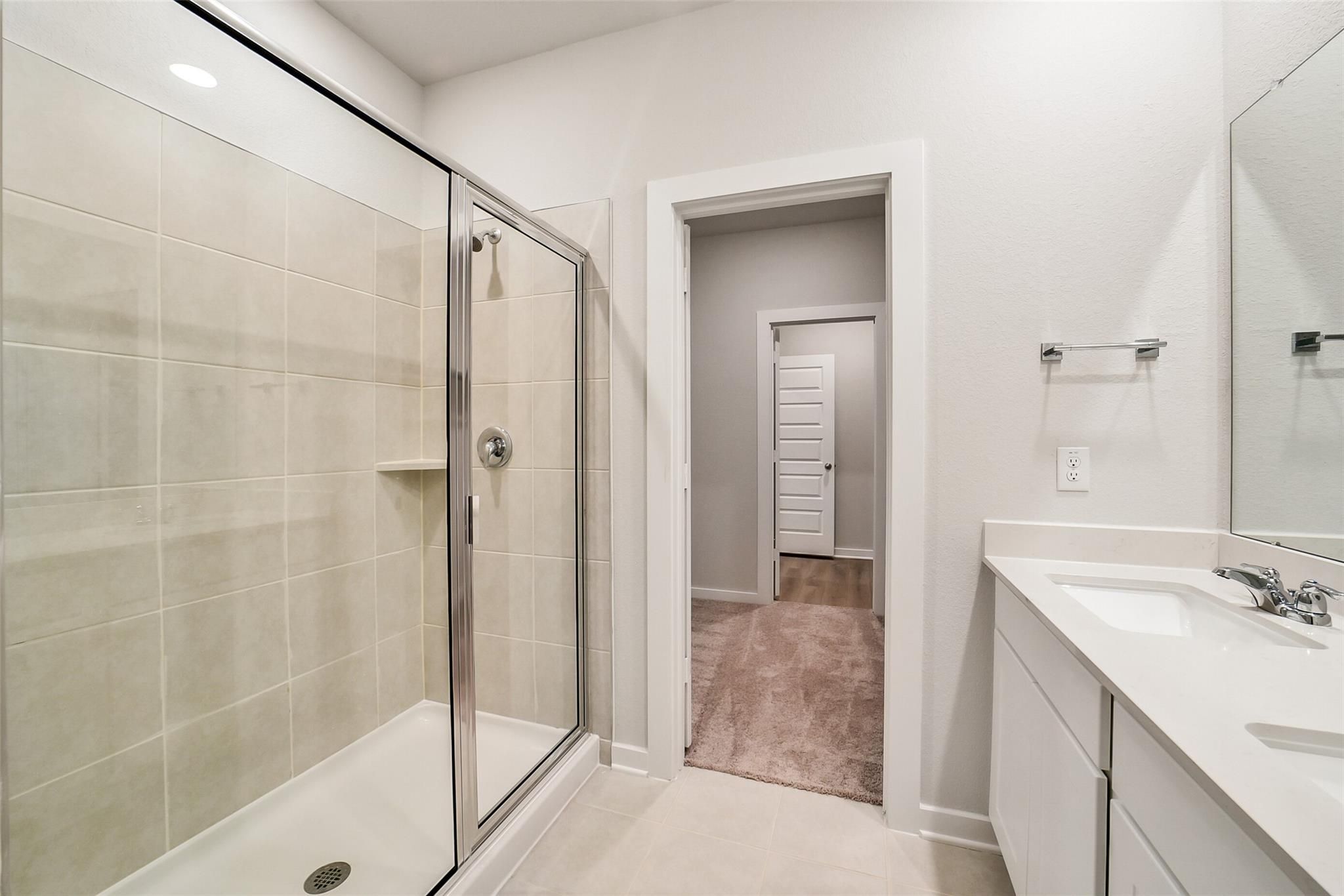 Elegant master bathroom with glass shower enclosure, beige tile, double vanity in Davidson Homes The Blanco E, Magnolia TX