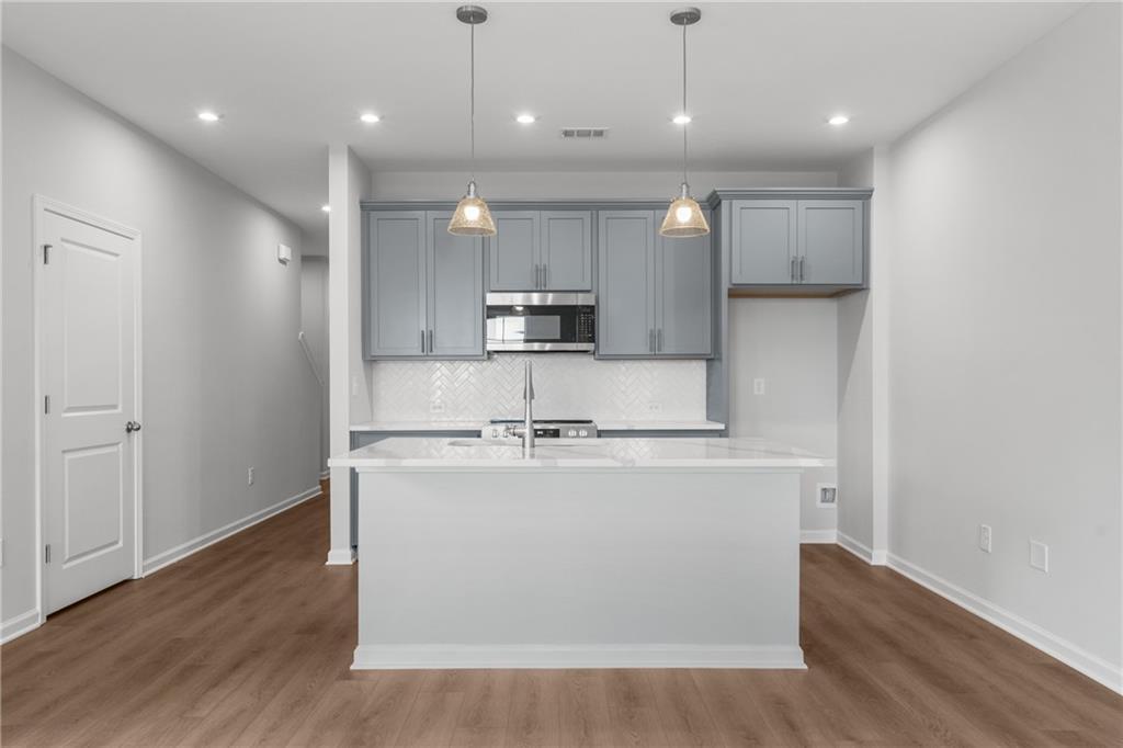 Modern kitchen featuring gray shaker cabinets, white quartz island, stainless steel appliances, subway tile backsplash in Davidson Homes The Monroe B, Emerson, GA