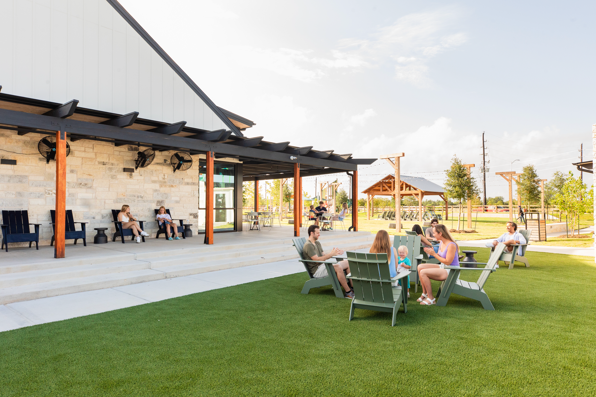 Outdoor pavilion at Emberly in Beasley TX with stone accents, Adirondack chairs on green lawn, residents relaxing under covered porch