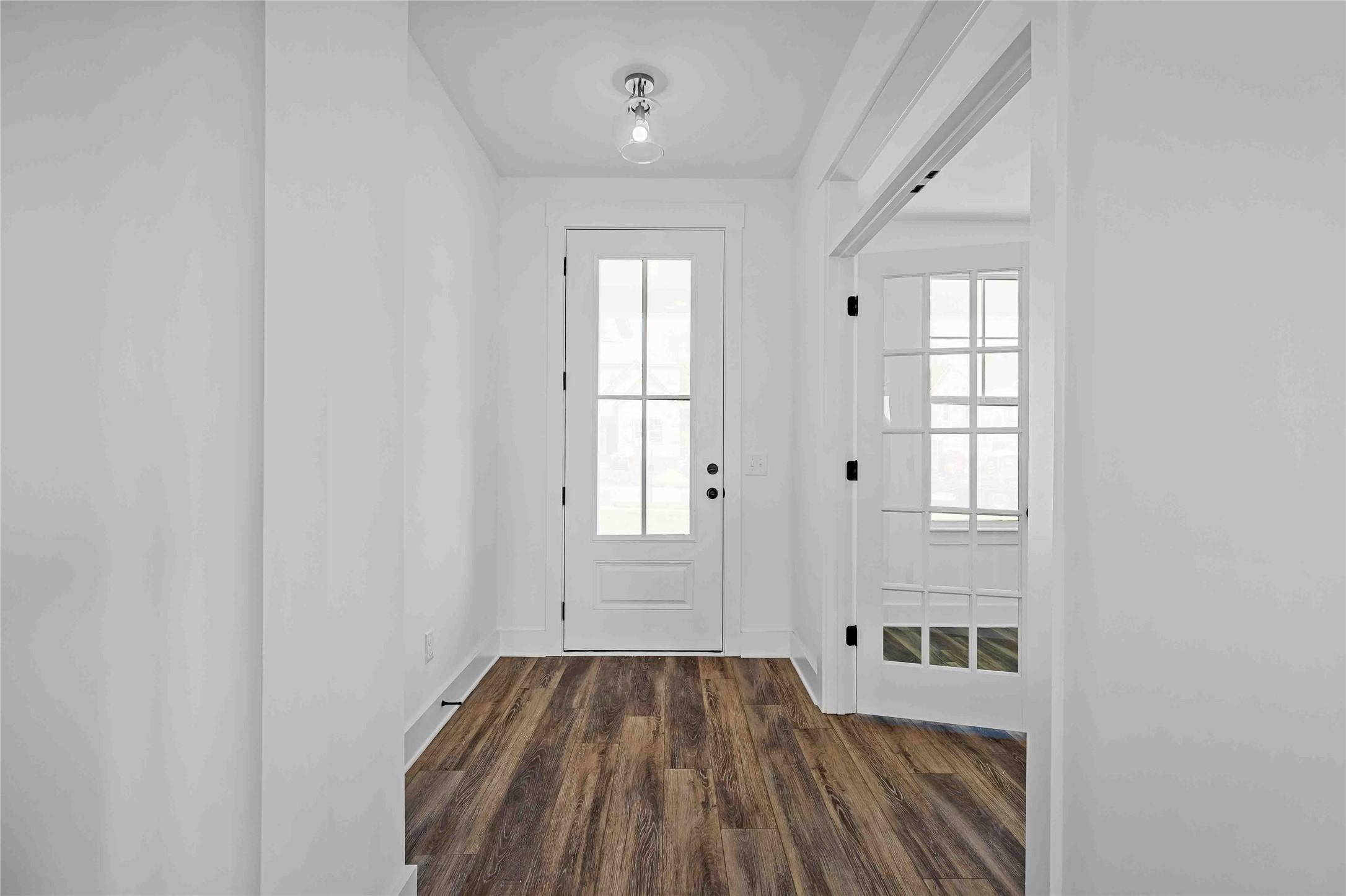 Bright entryway with wood-look flooring and glass-paneled doors in The Ash O floor plan by Davidson Homes in Heartland, TX.