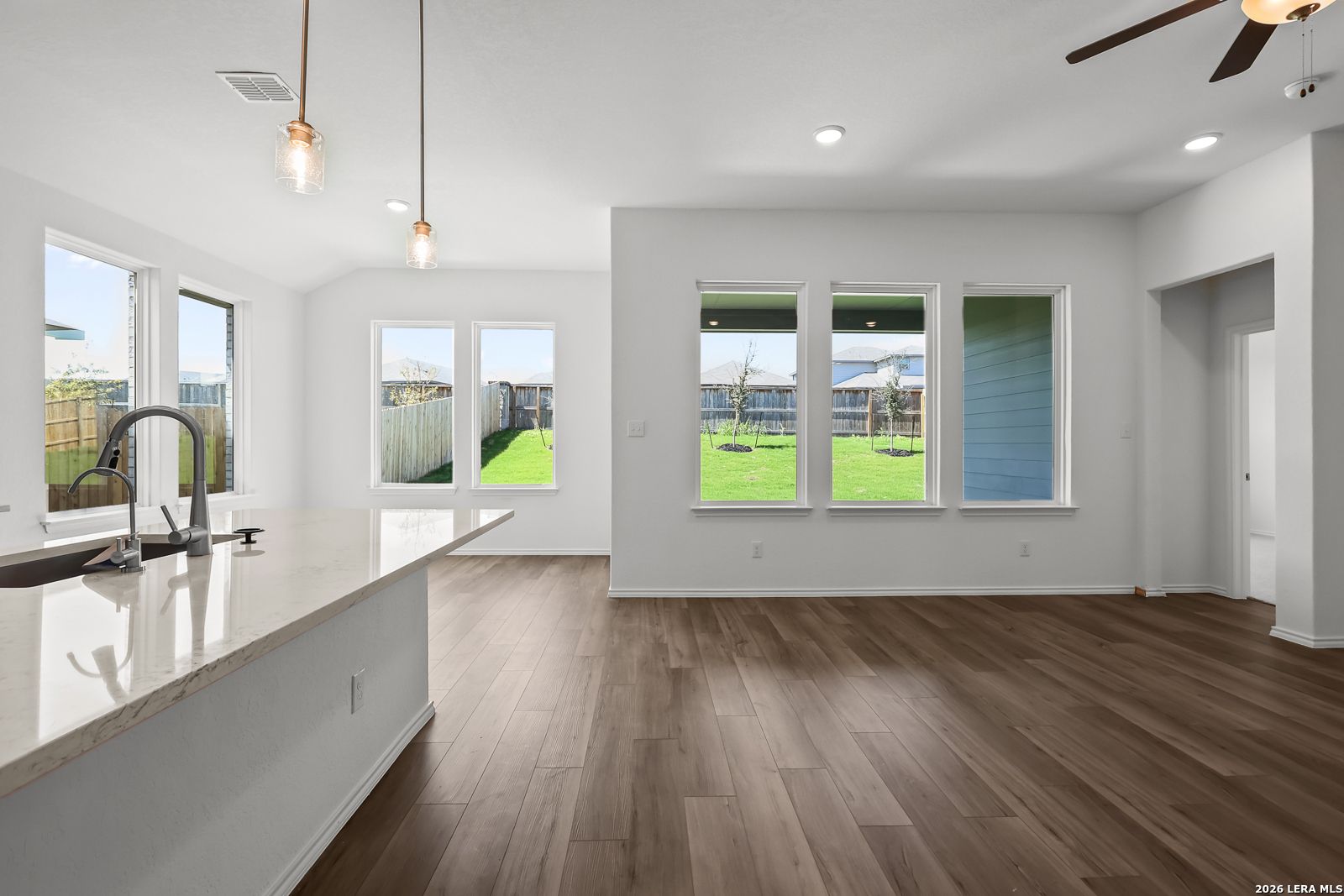 Bright open kitchen with white island, pendant lights, and large windows to lush backyard in Davidson Homes Sequoia B, San Antonio