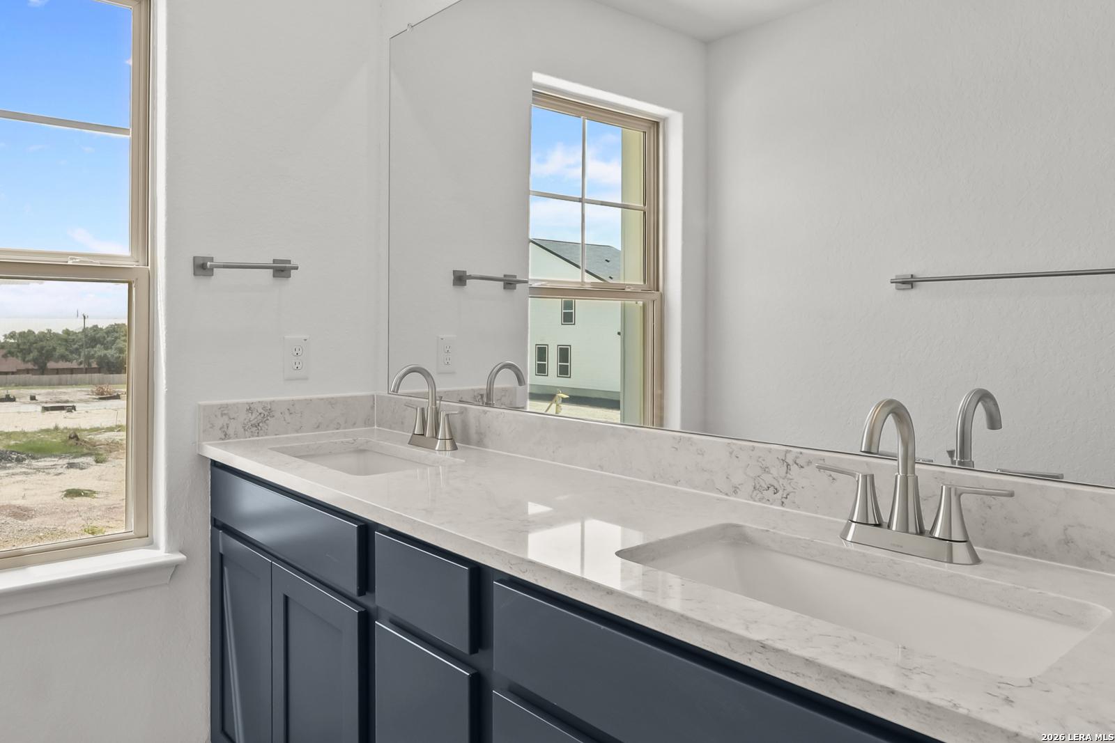Modern double vanity with quartz countertops and navy cabinets in The Gillian C home at Meadows at Oak Creek, San Antonio.