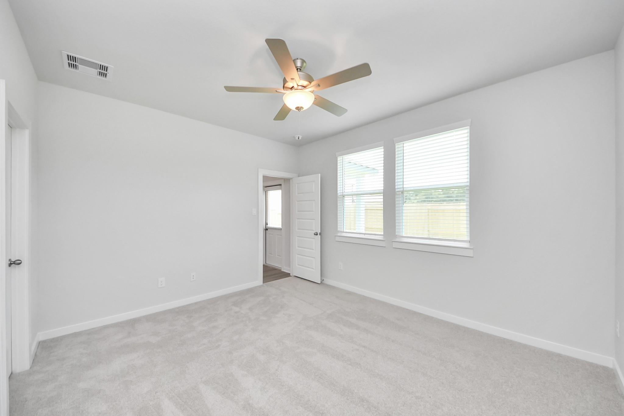 Bright, carpeted bedroom with ceiling fan in The Frio F floor plan at Liberty Estates in Cleveland, Texas.