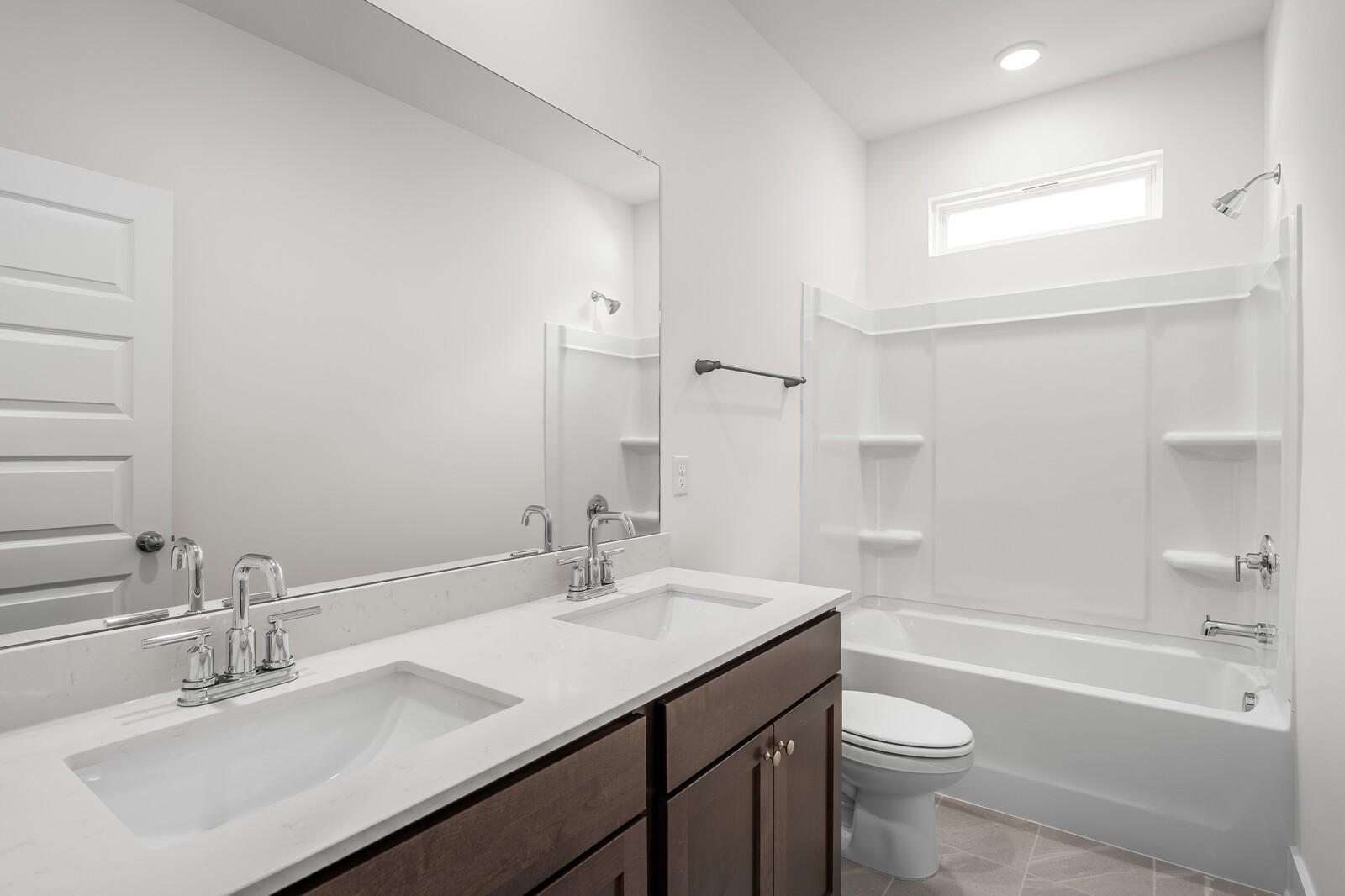 Modern bathroom with dual vanity, white countertops, and tub-shower combo in The Cottonwood E, Woods Crossing, Gallatin, TN.