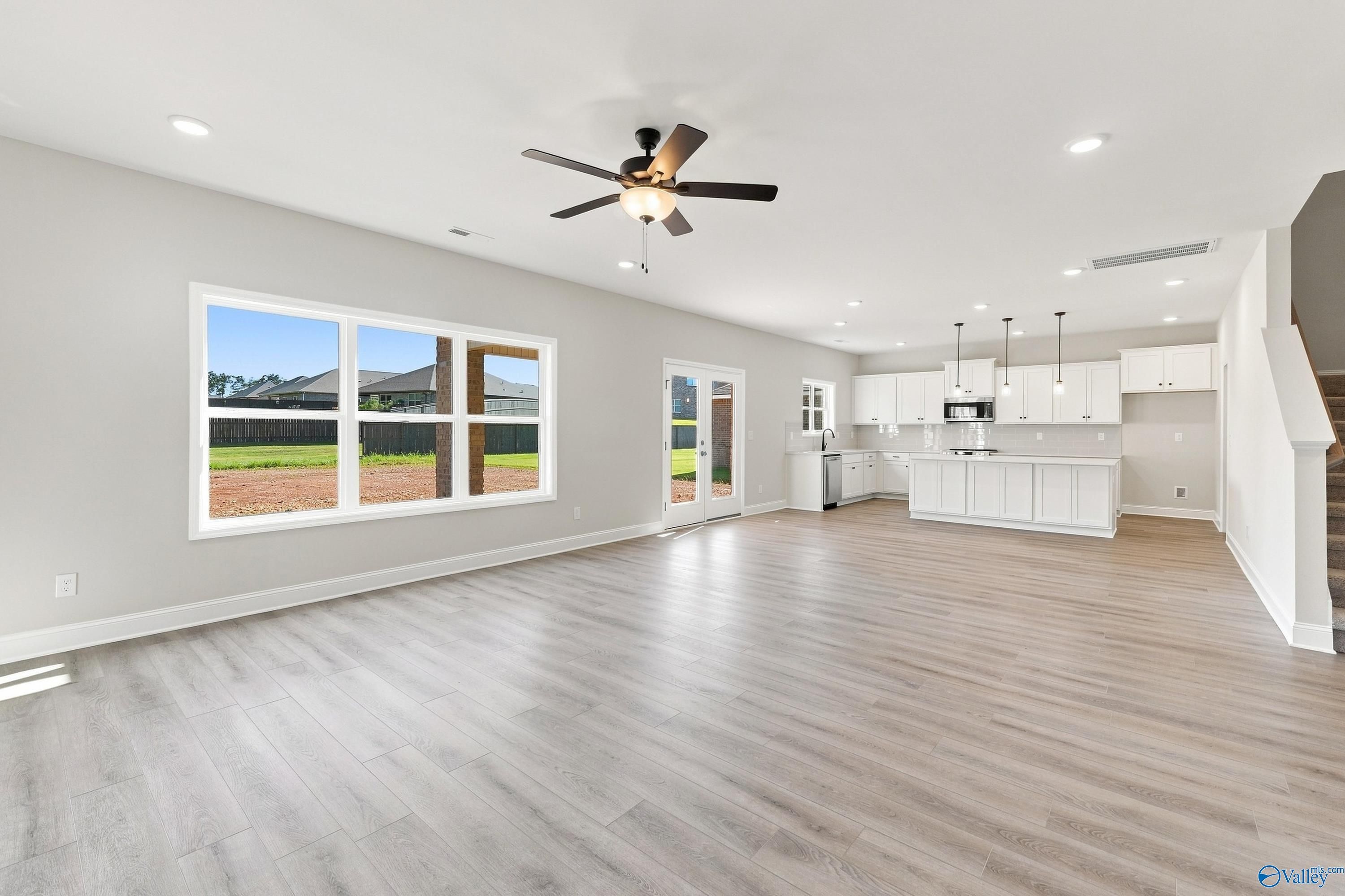 Open-concept living room and kitchen with luxury vinyl plank flooring, white cabinetry, and ceiling fan in Davidson Homes Chelsea B floor plan.