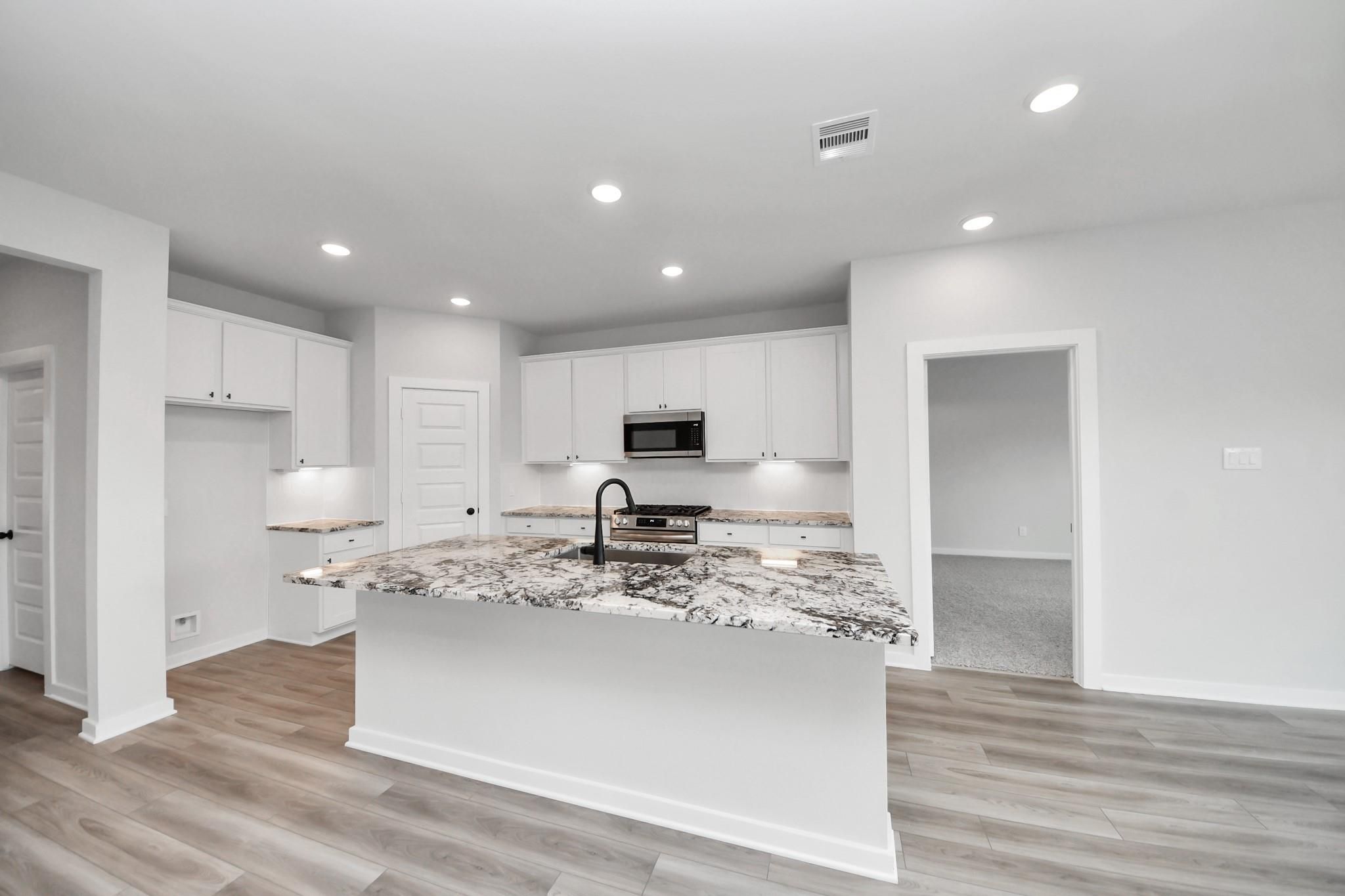 Modern kitchen with marble-patterned island, white cabinets, and stainless appliances in The Everett C, Dayton, Texas home.