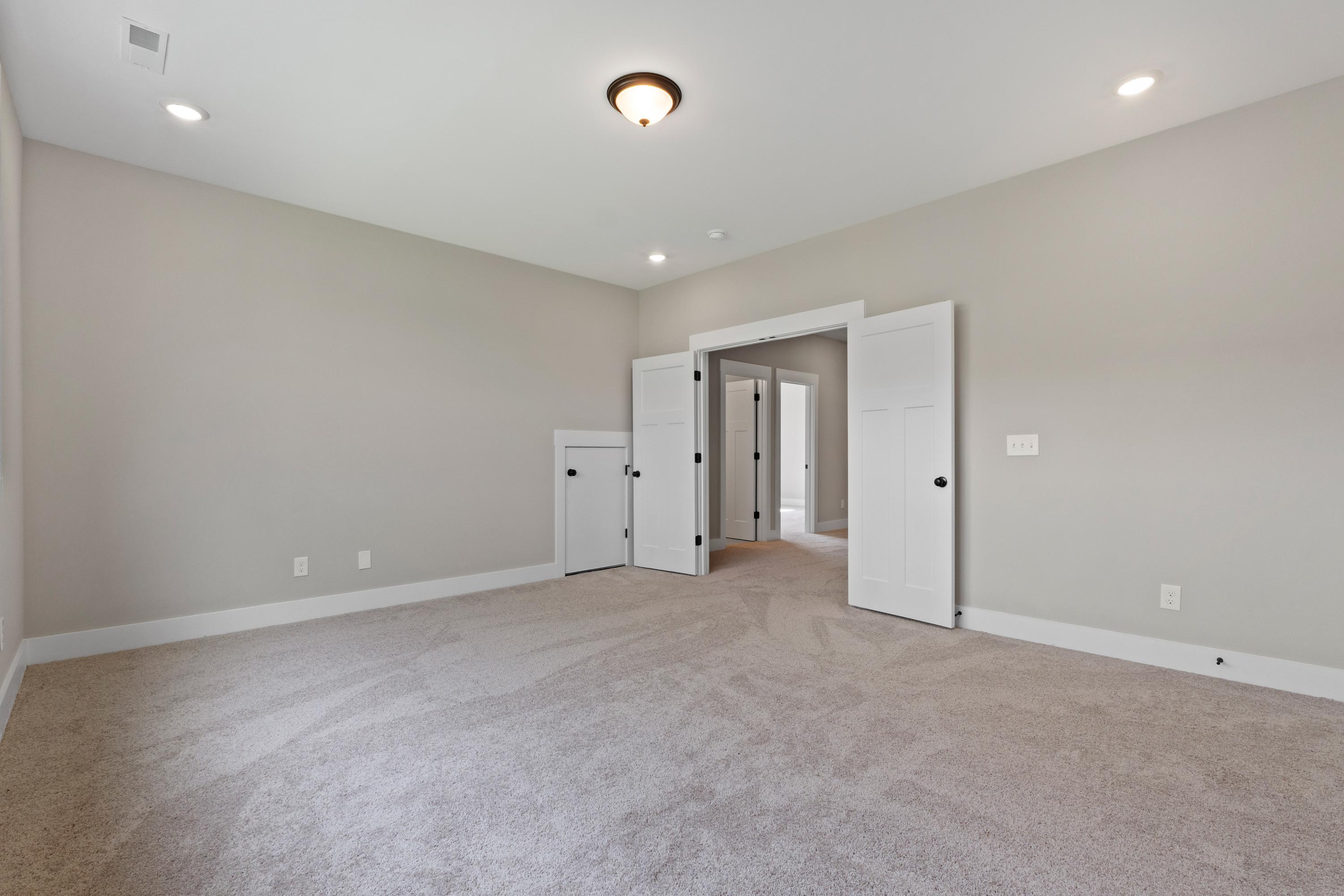 Spacious upstairs bedroom in The Oxford home design with beige walls, carpeted floor, recessed lights, and open double doors