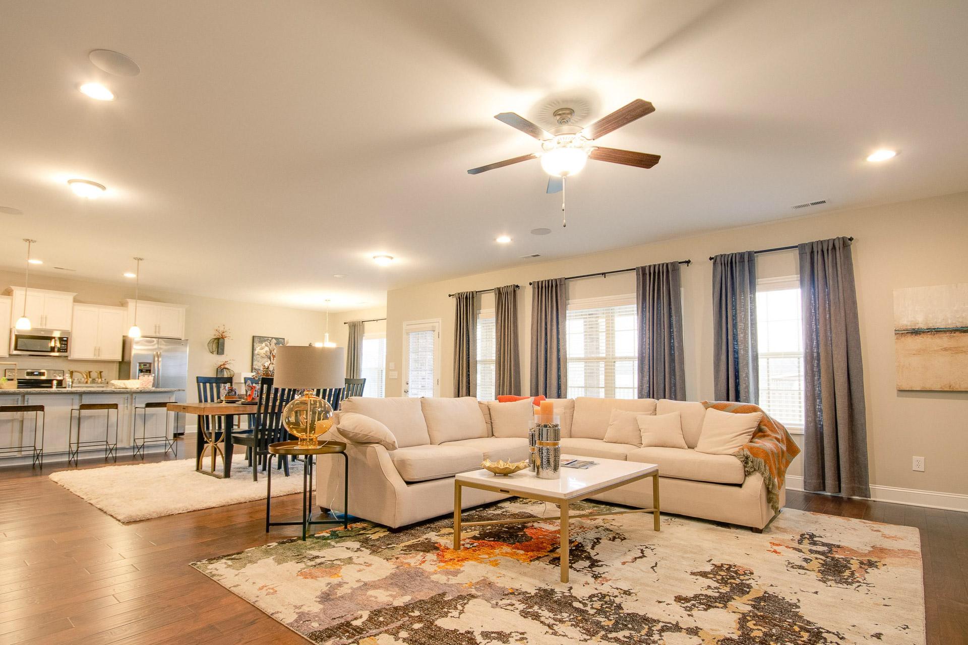 Spacious open-concept living room in Summer Pointe Madison AL home with L-shaped beige sofa, patterned rug, ceiling fan, and adjacent white kitchen island