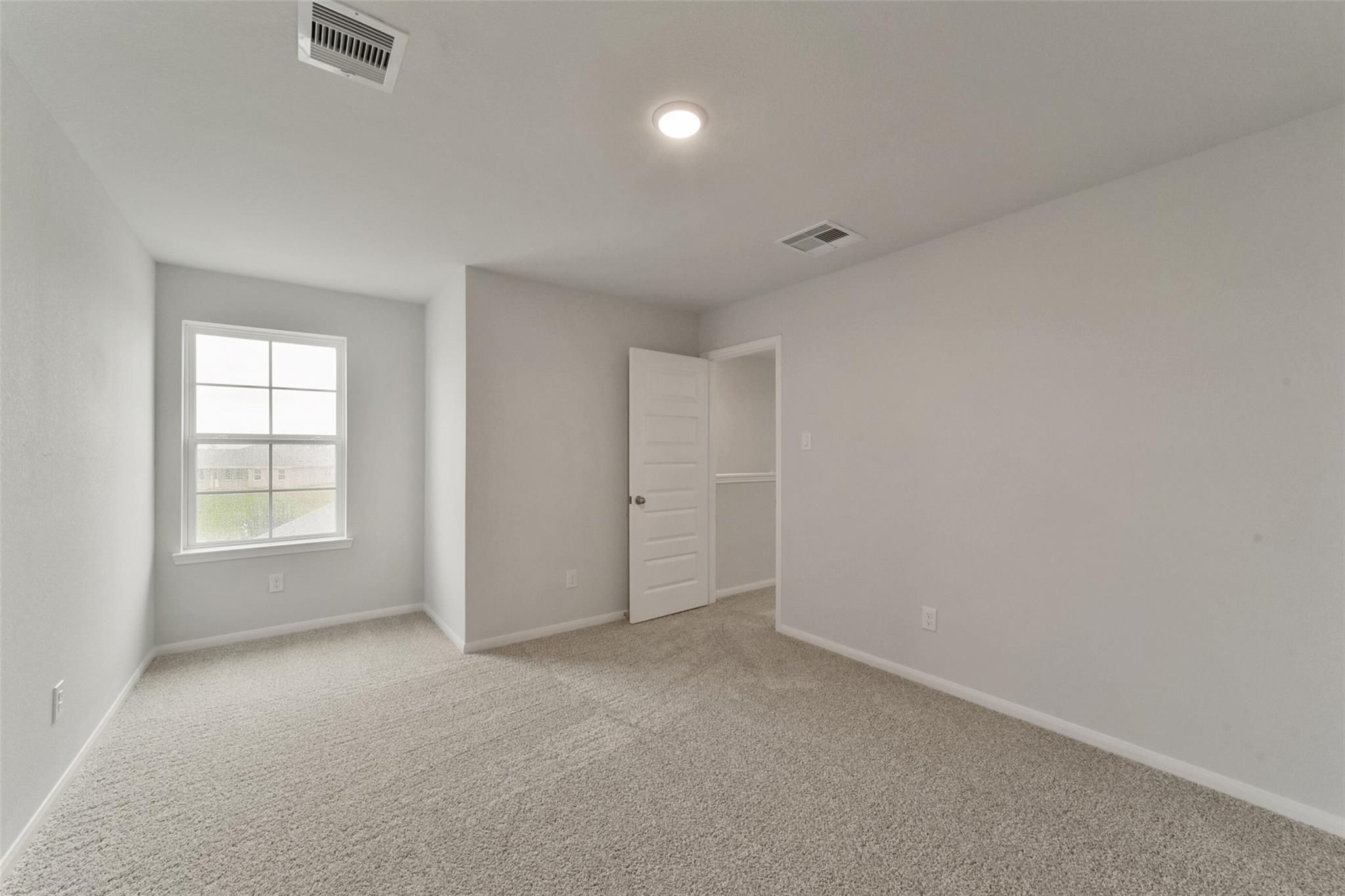 Spacious secondary bedroom with neutral gray walls, beige carpet, large window, and closet doors in Davidson Homes San Marcos E, Beasley, Texas