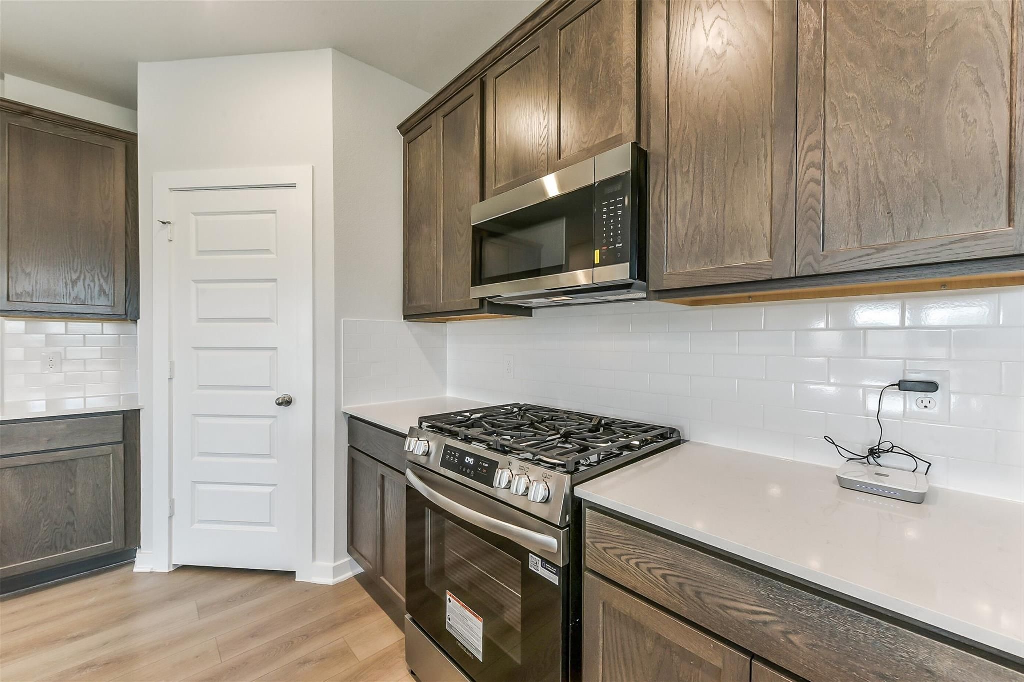 Modern kitchen with warm wood shaker cabinets, white subway tile backsplash, quartz counters, stainless gas range in The Sabine F, Dayton, Texas