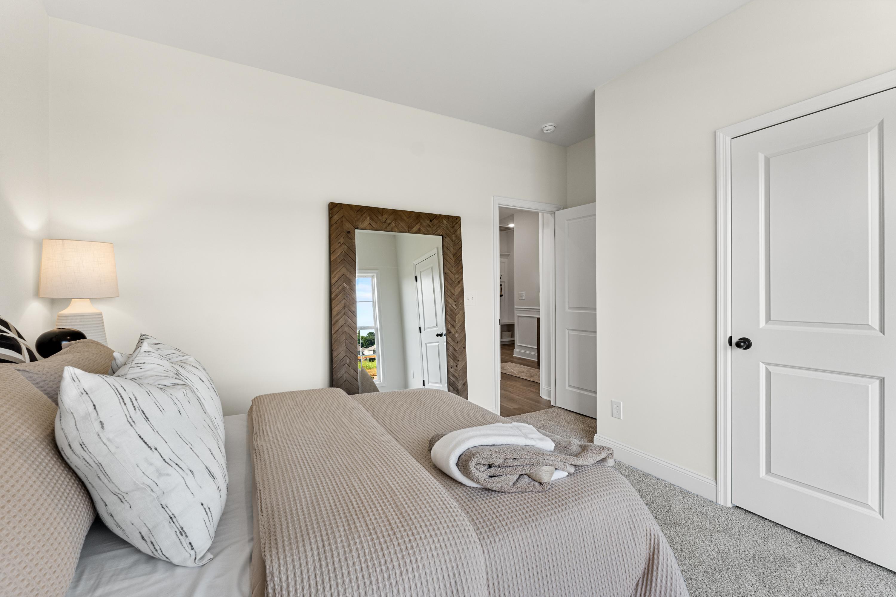 Primary bedroom at Lynn Meadows in Meridianville AL with king bed neutral bedding large framed mirror and beige walls