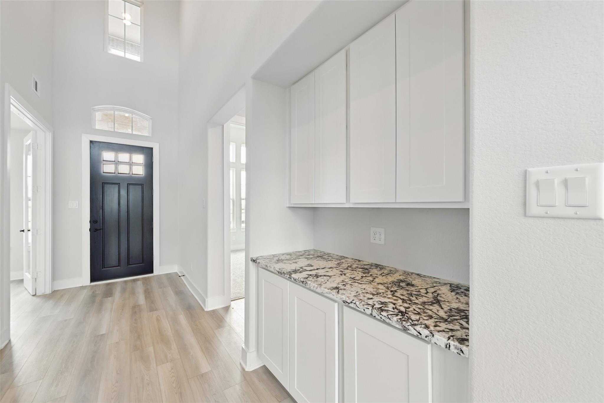 Grand entry foyer with dark wood door, hardwood floors, white cabinets, and granite countertop in Davidson Homes The Victoria C, Lago Mar, Texas City