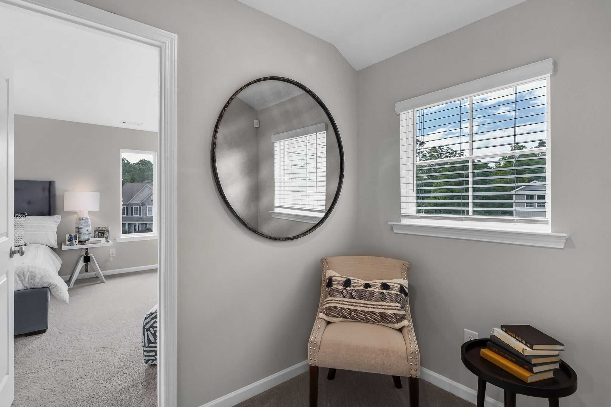 Cozy bedroom interior at Ivy Glen in Perry Georgia featuring round wall mirror, beige armchair, and window with tree view