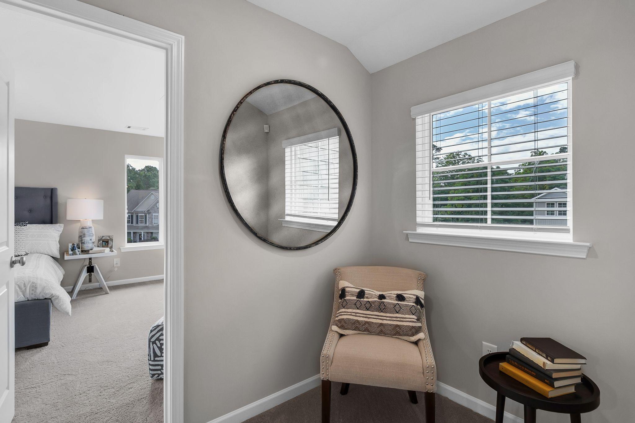 Cozy bedroom interior at Ivy Glen in Perry Georgia featuring round wall mirror, beige armchair, and window with tree view