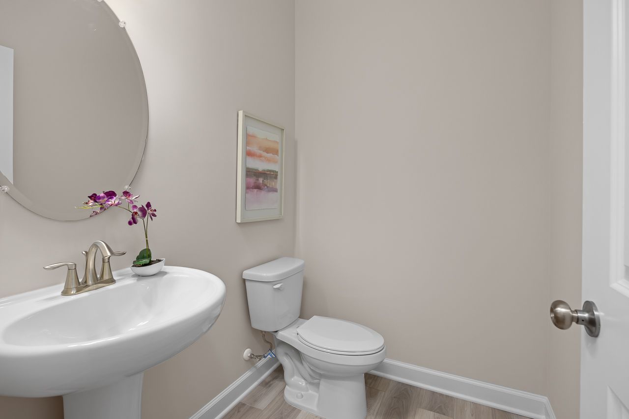 Modern powder room in The Chestnut home design featuring a pedestal sink, round mirror, and neutral wall tones.