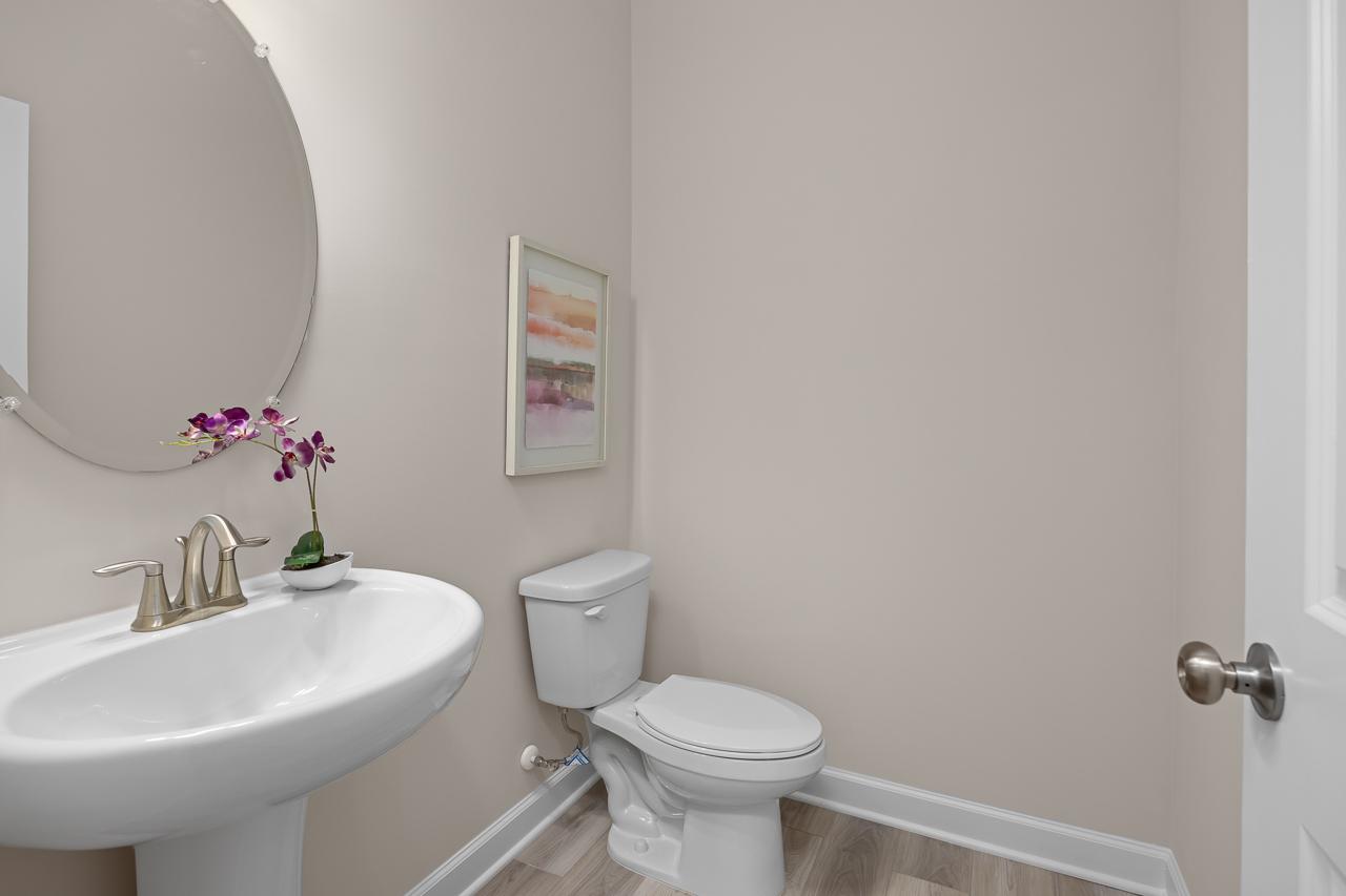 Modern powder room in The Chestnut home design featuring a pedestal sink, round mirror, and neutral wall tones.